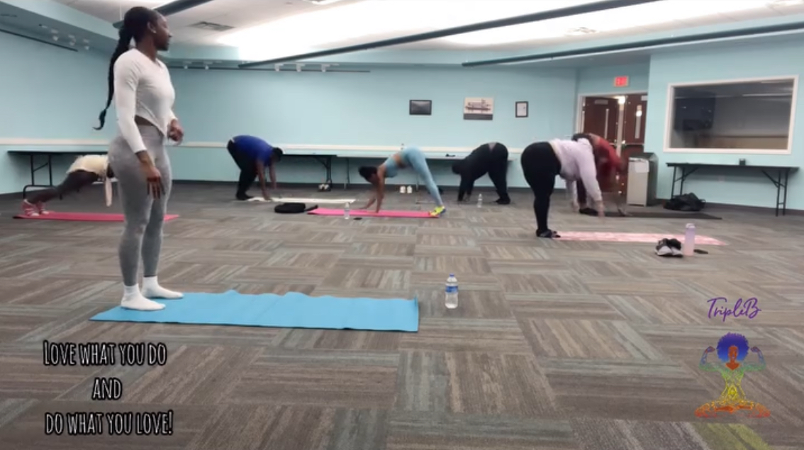 Group of people participating in a fitness class in a spacious room with mats and water bottles on the floor.