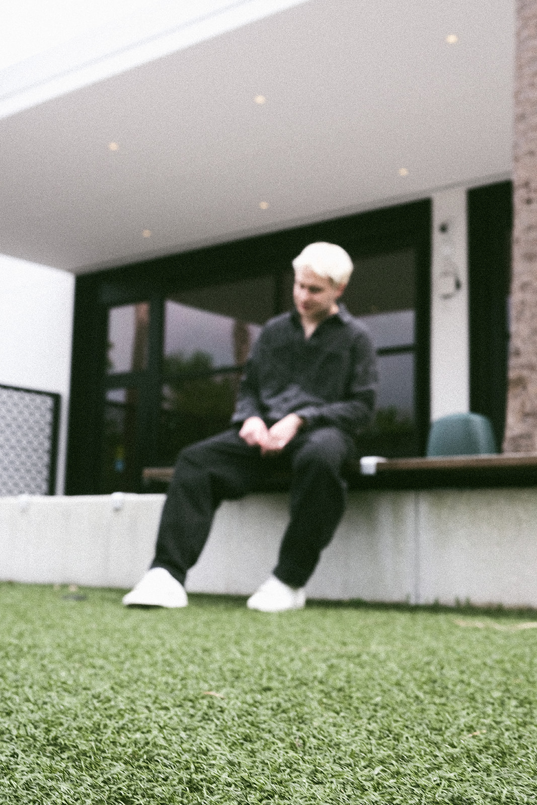 Person with white hair sitting on a concrete ledge outside a building with large windows.