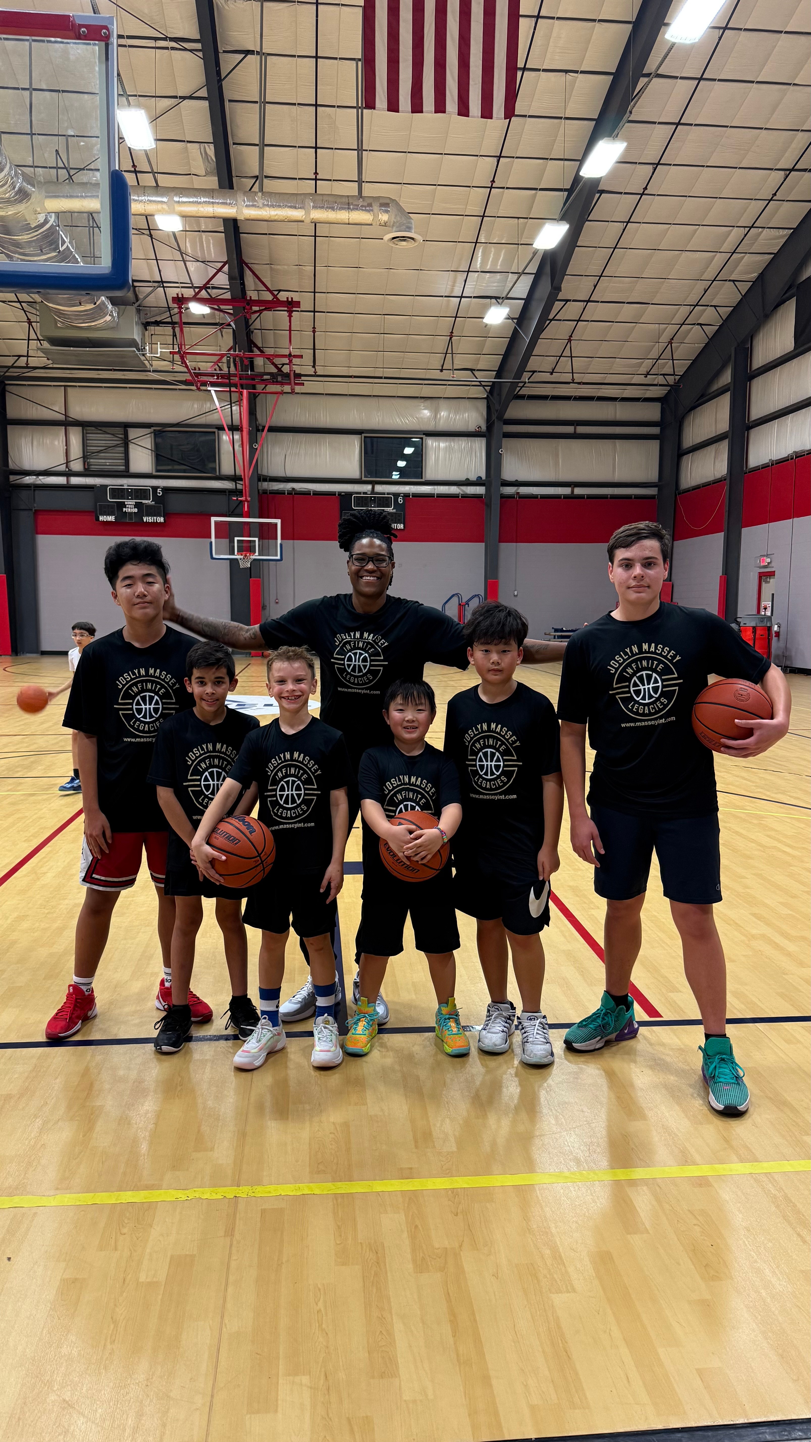 Group of seven children and two adults standing in a basketball court, holding basketballs, smiling.
