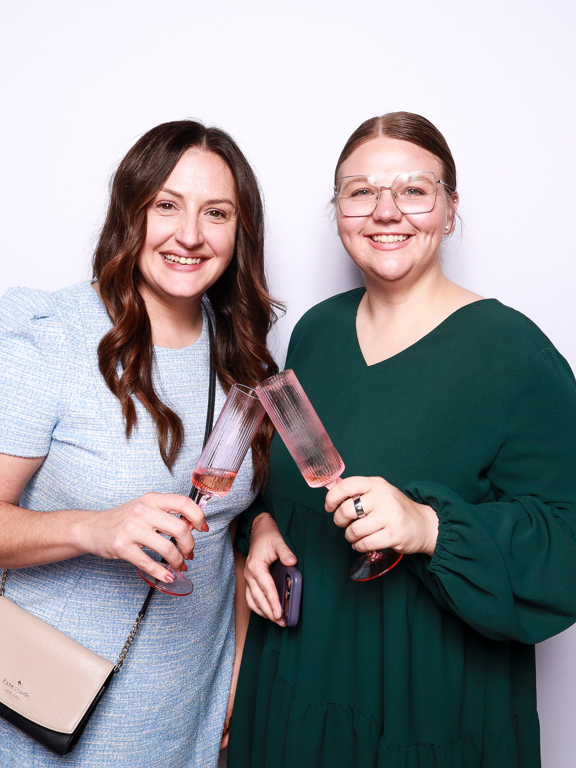 Two women smiling and holding glasses of champagne, standing against a white background.