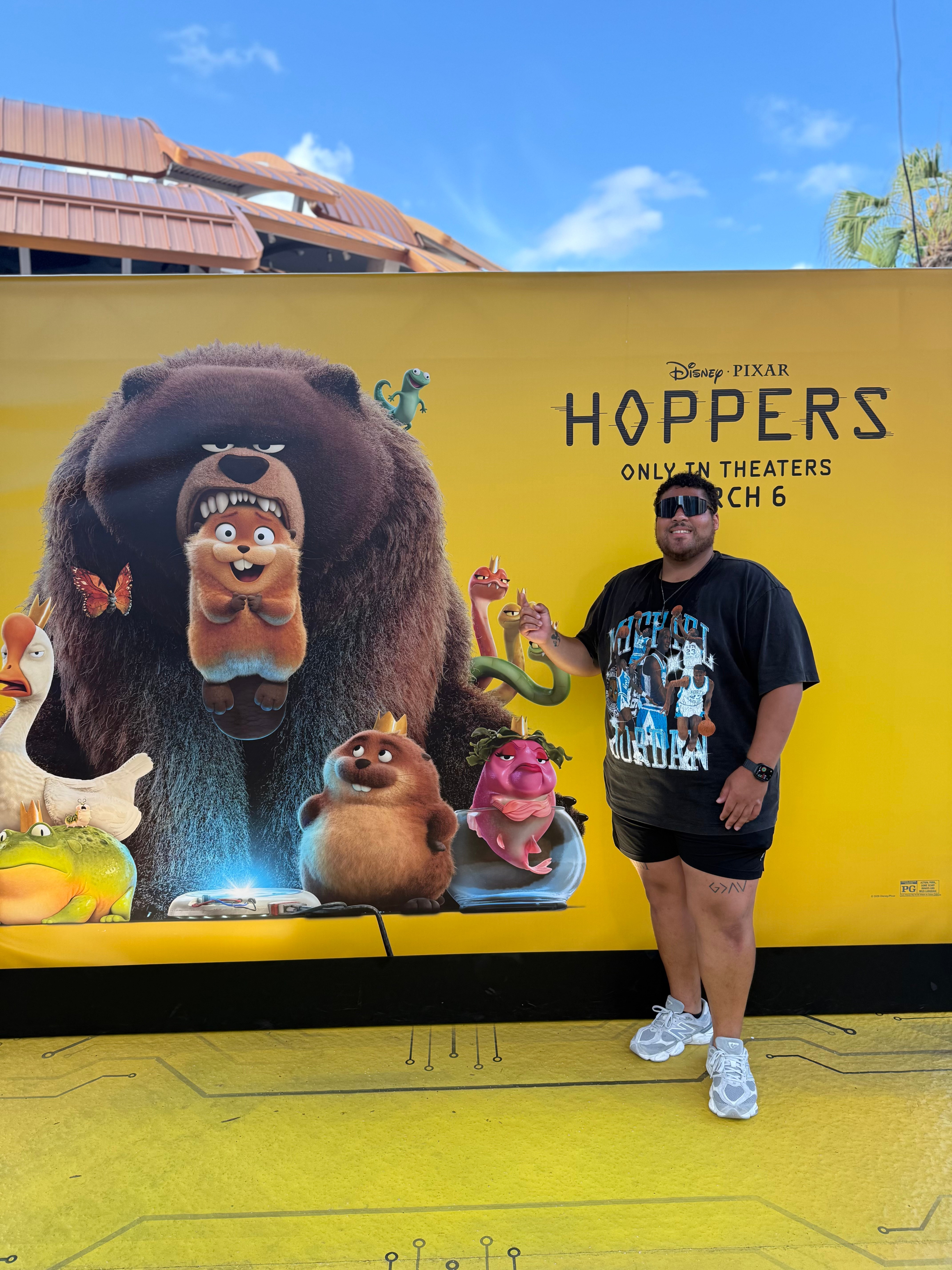 Person standing in front of a large promotional poster for Disney Pixar's 'Hoppets' with animated characters, yellow background.