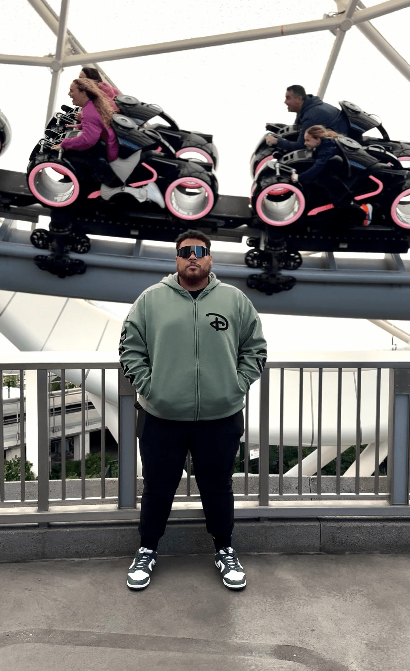 Person standing in front of an amusement park ride with two people on a roller coaster above him.