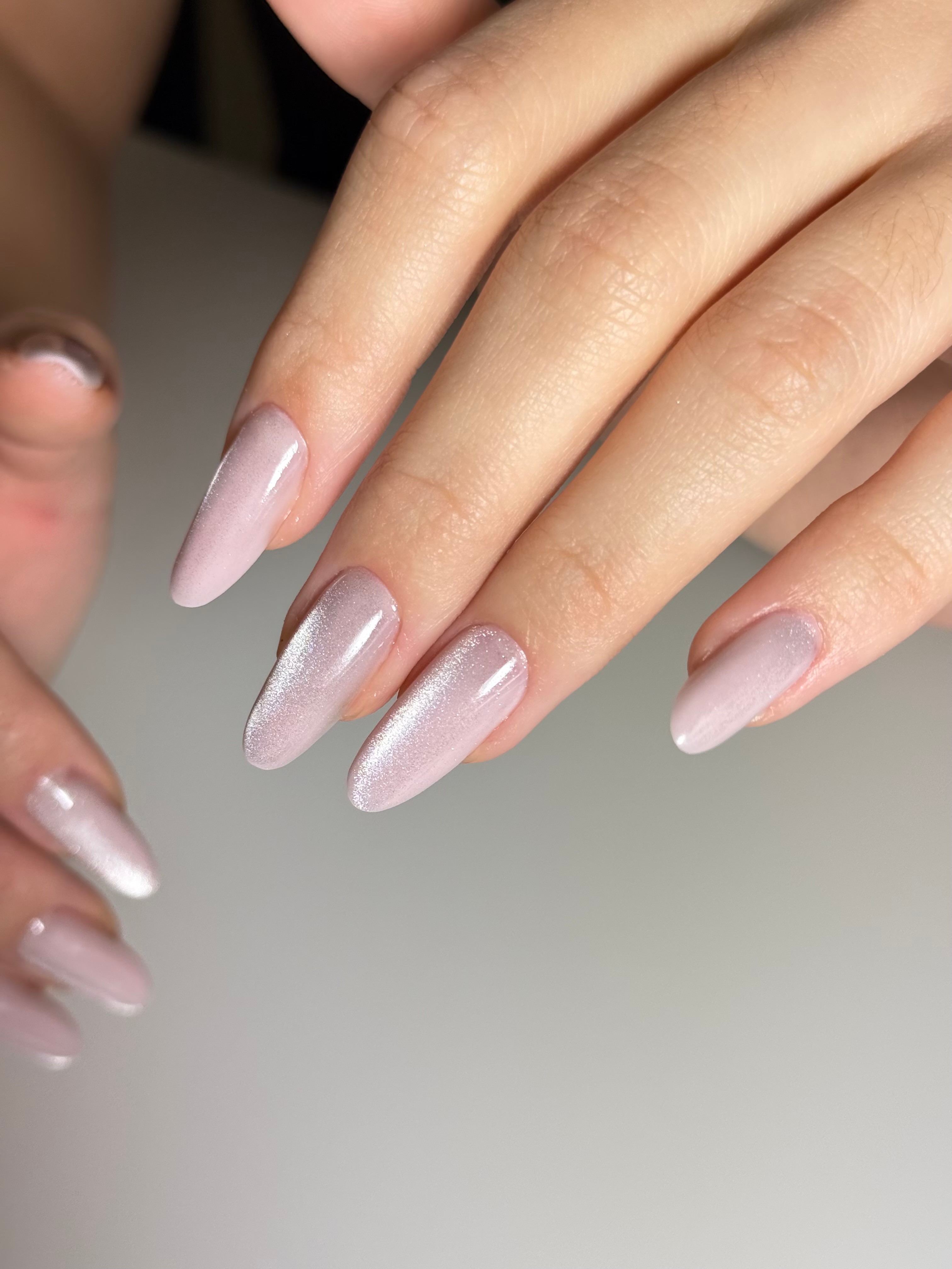 Close-up of well-manicured nails with light pink and clear polish on fingers, against a neutral background.
