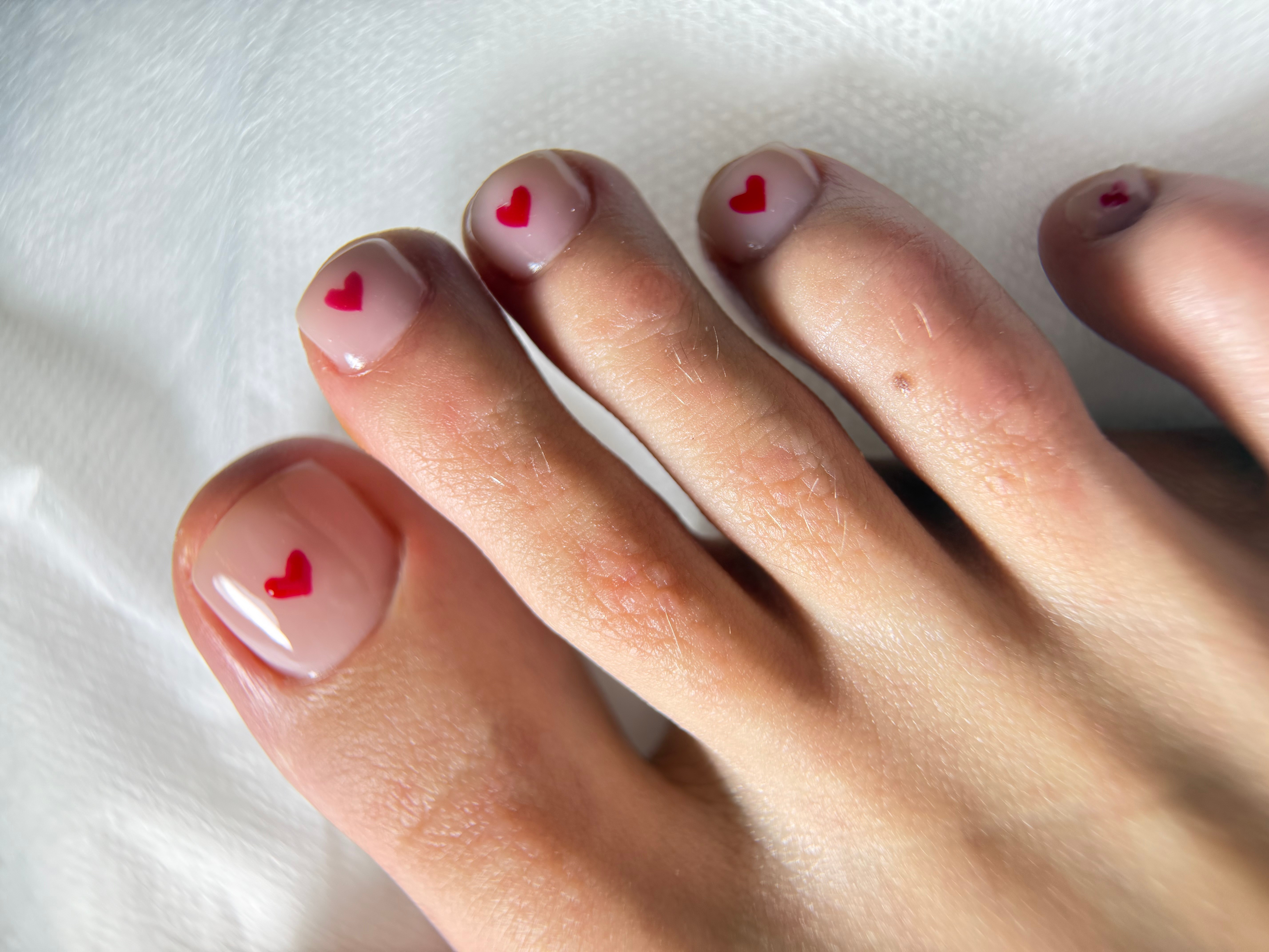 Close-up of toes with nail art featuring small red hearts on a light background.