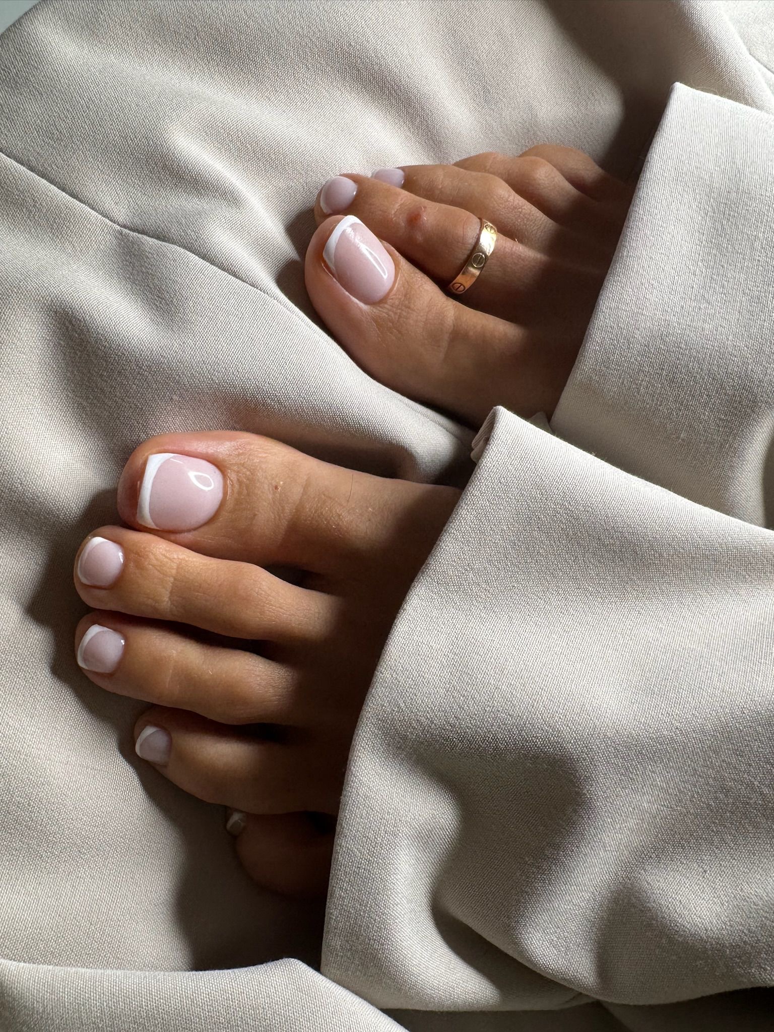 Person's hands with manicured nails and a ring, holding a beige fabric garment.