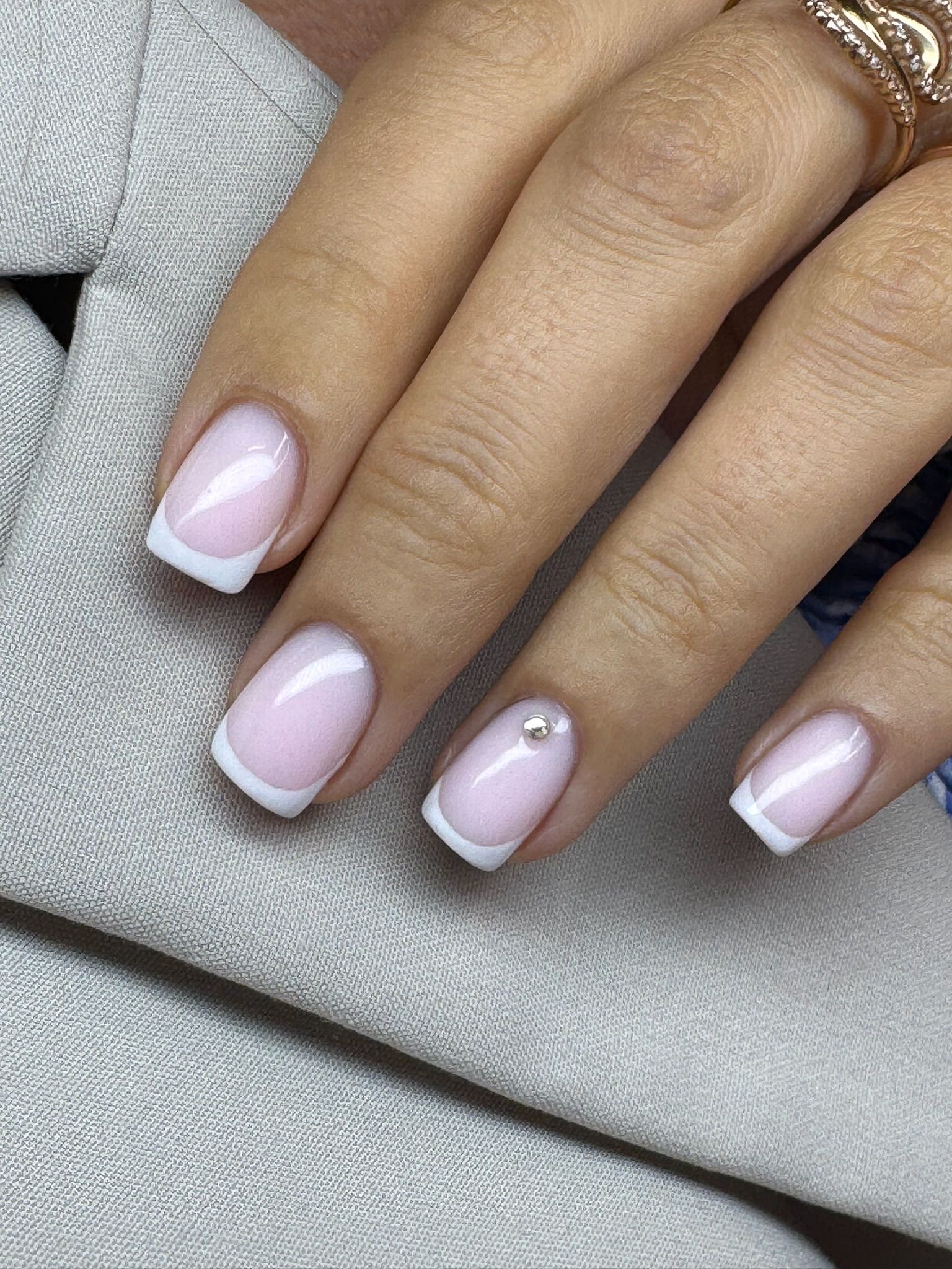 Close-up of a hand with manicured nails featuring French tips and a small pearl decoration, resting on fabric.