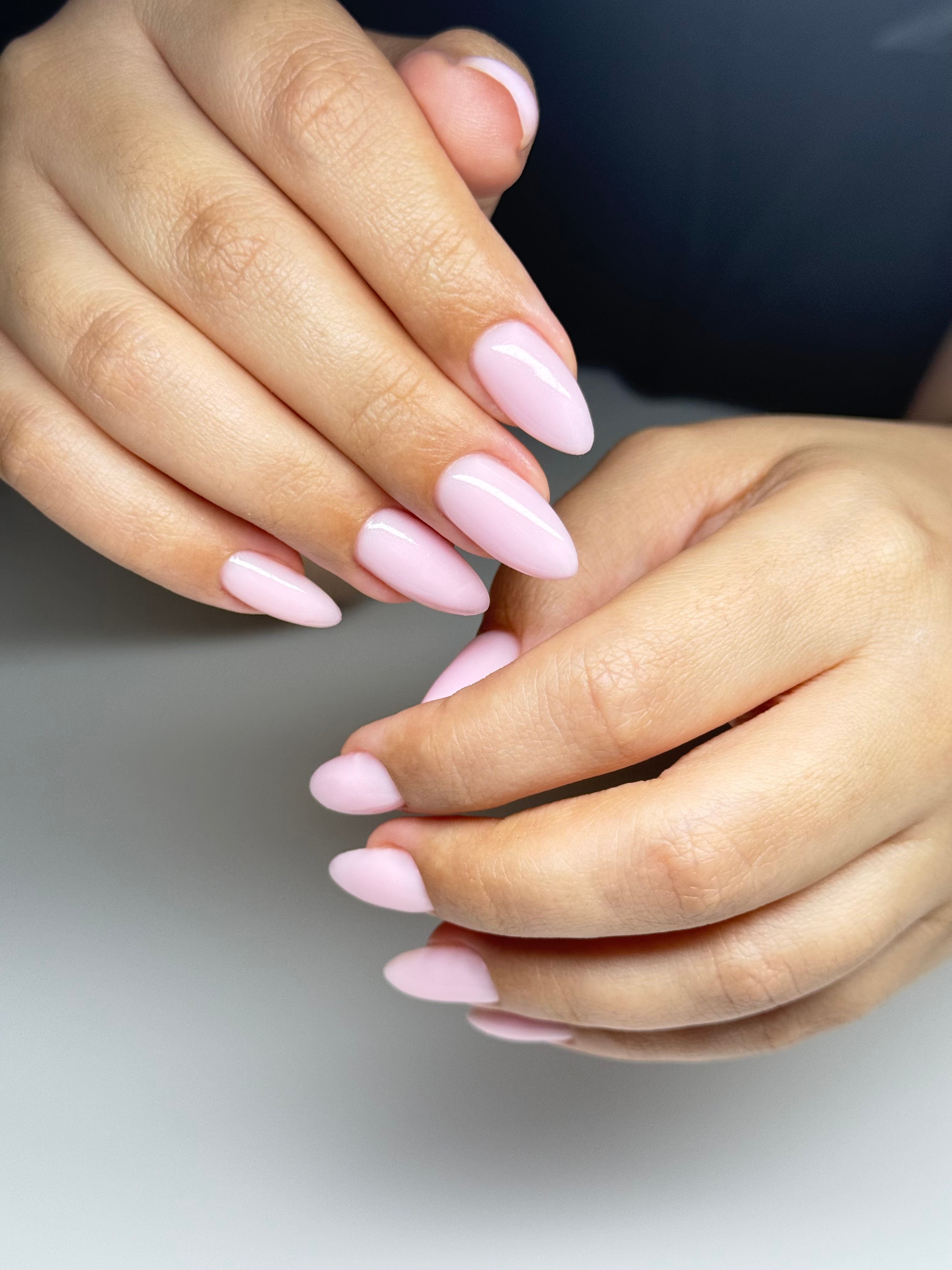 Close-up of hands with light pink, oval-shaped manicured nails resting on a surface.