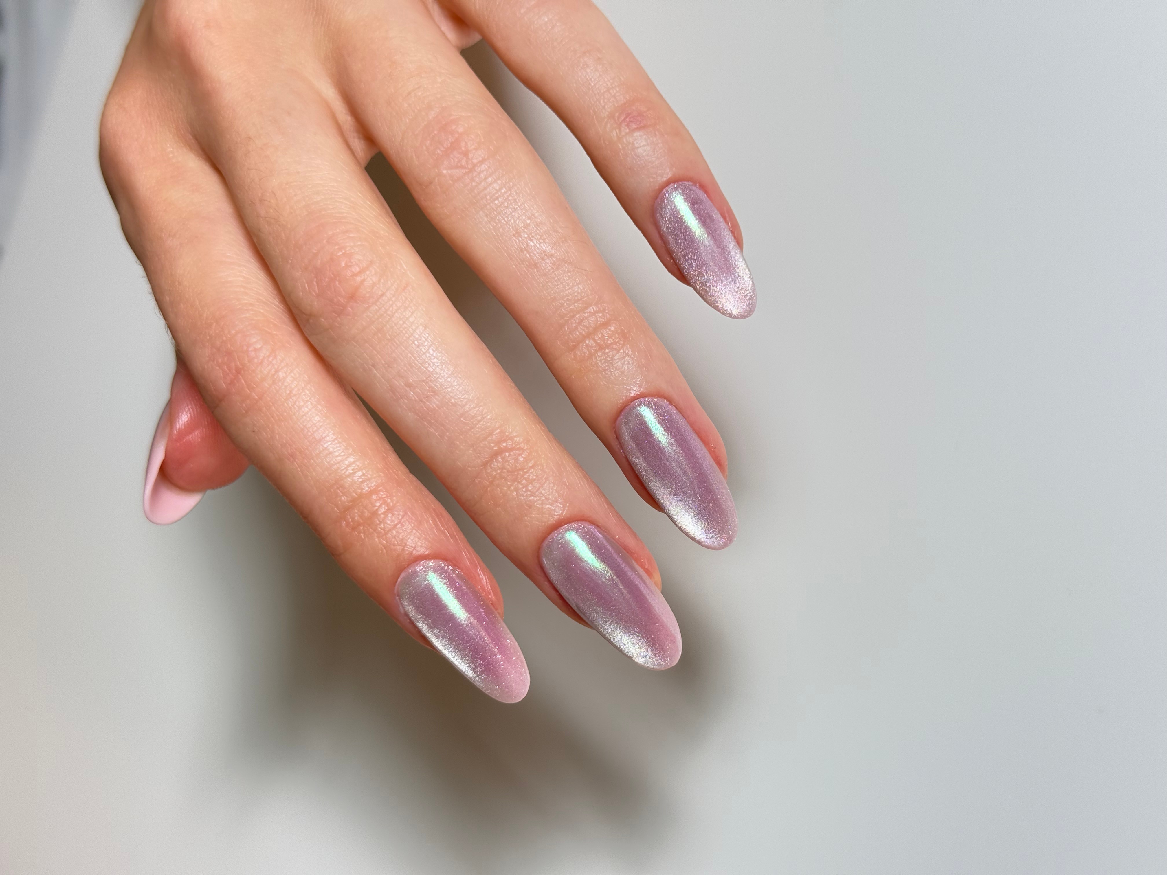 Hand with nails painted in iridescent pink and silver, fingers slightly curved, against a plain background.