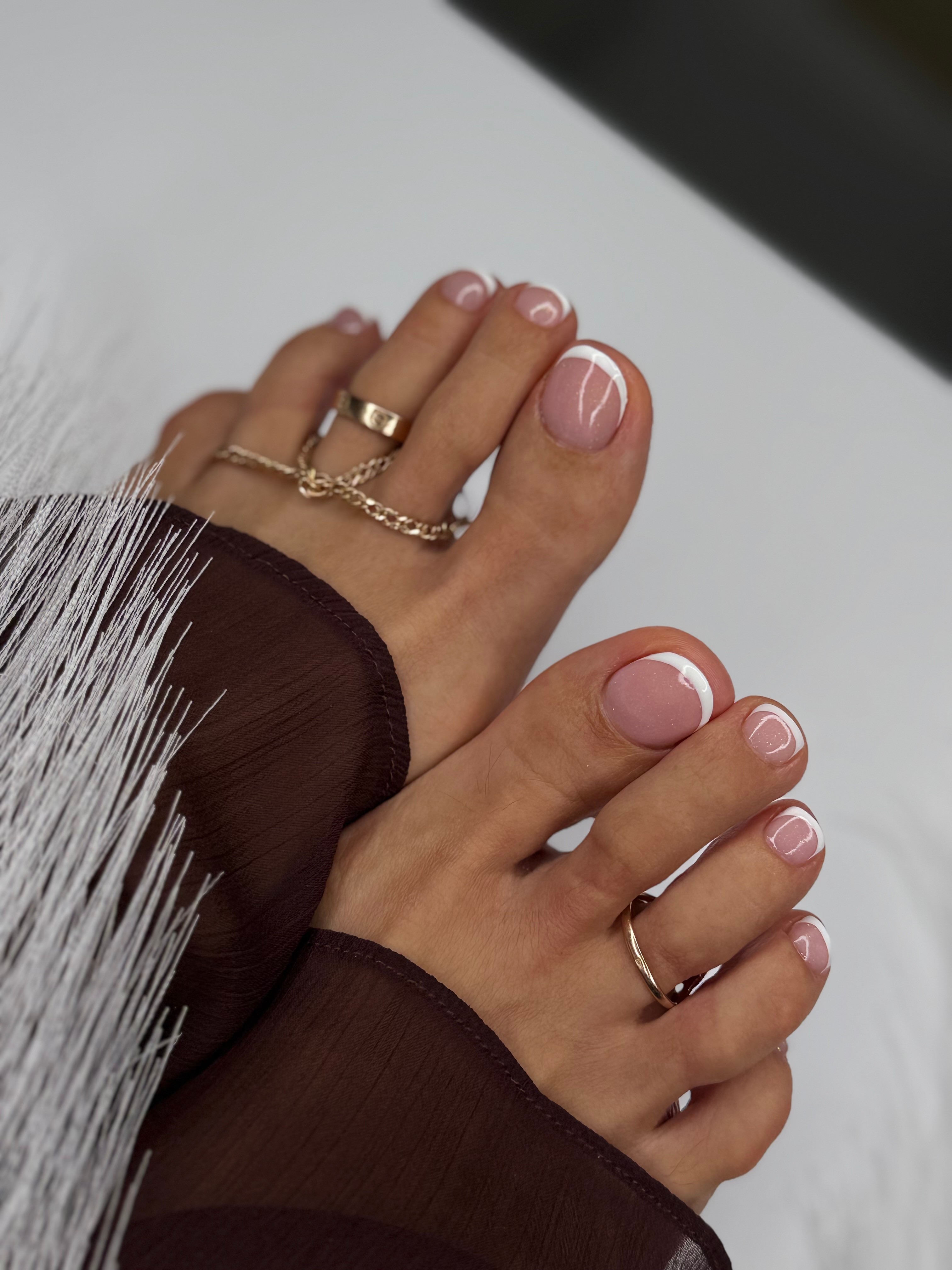 Two hands with rings and manicured nails, resting on a surface, wearing dark long sleeves.