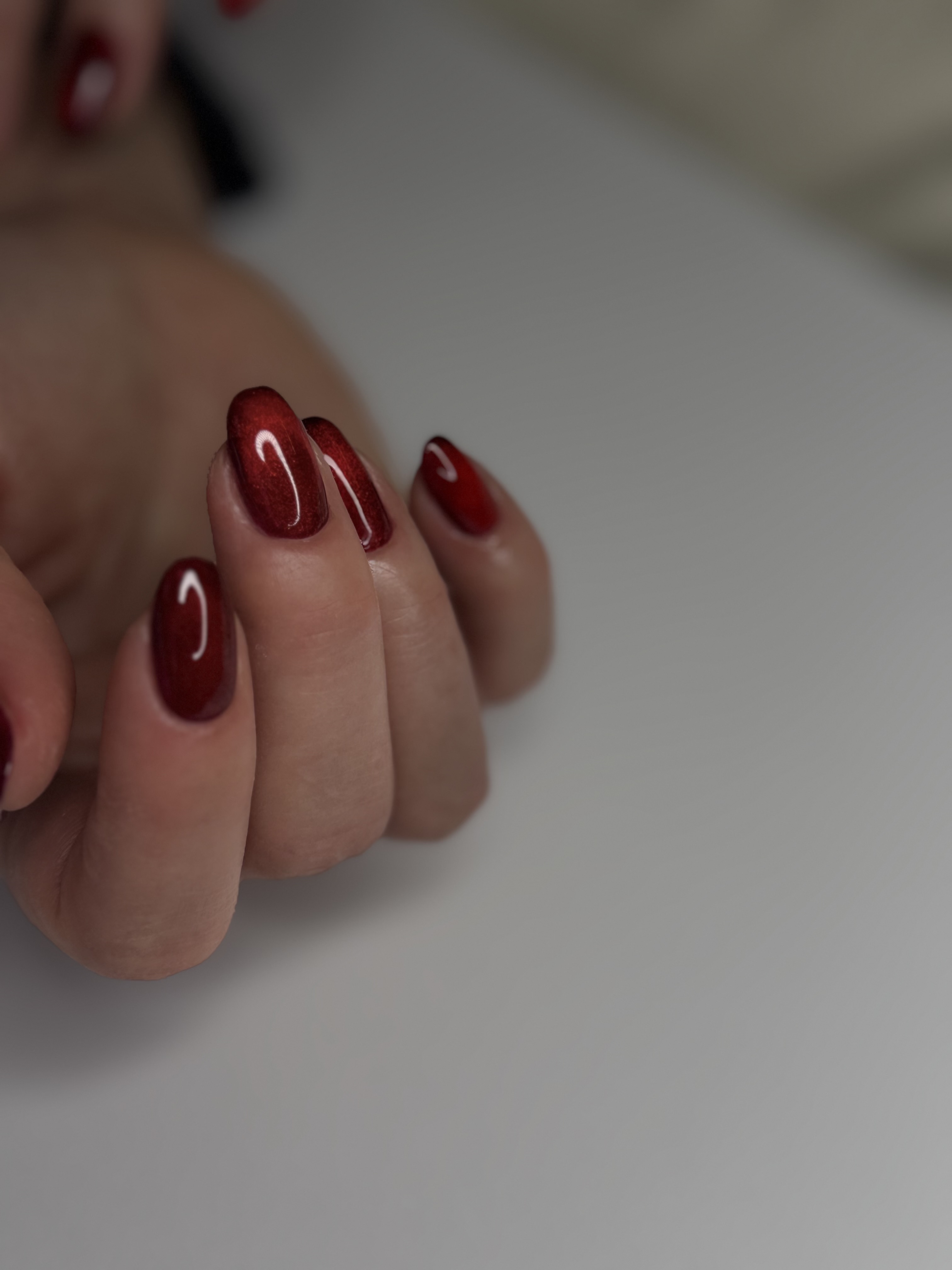 Hand with red painted nails resting on a white surface, fingers slightly curled, background blurred.