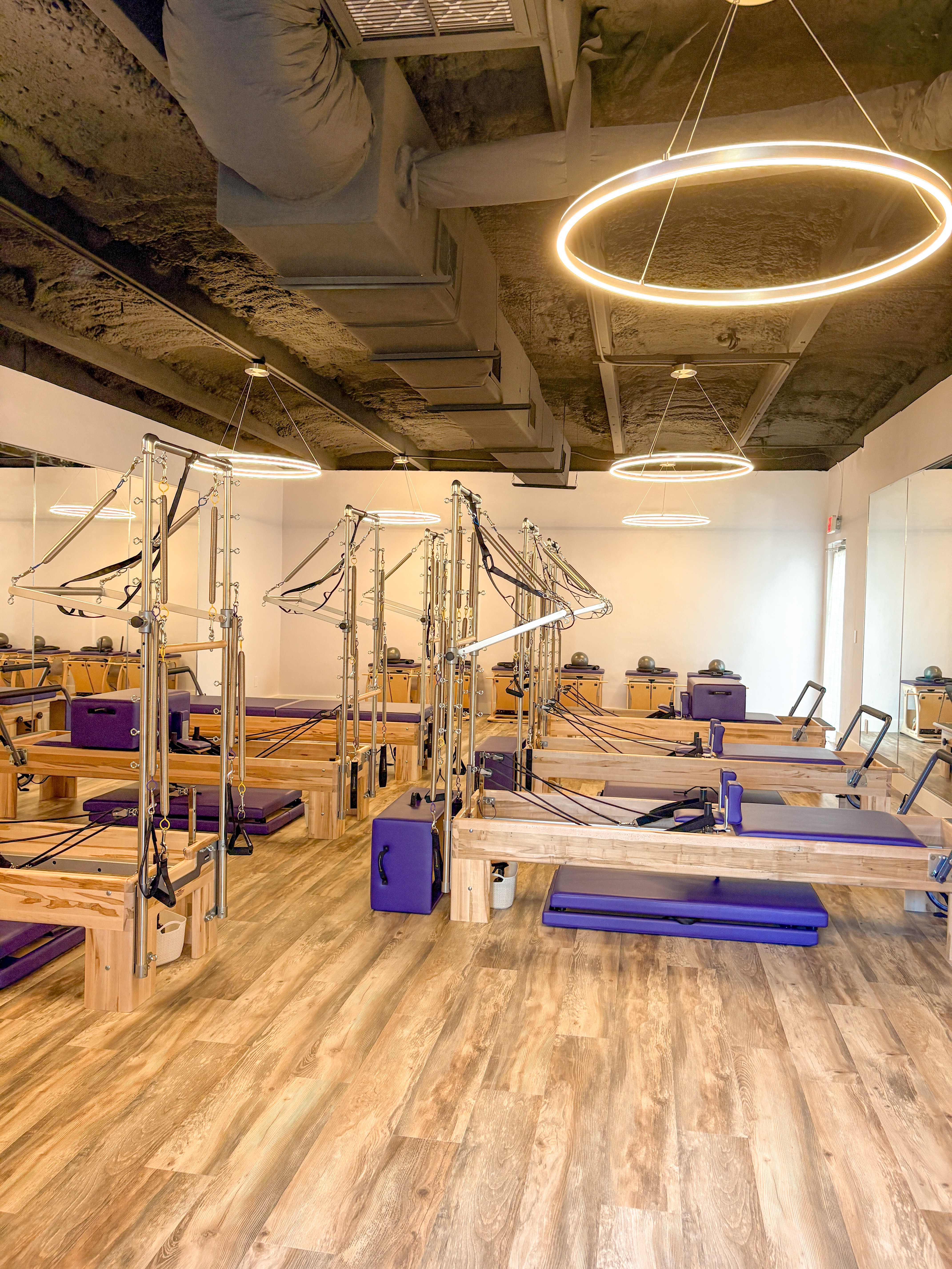 Pilates studio with reformer machines, wooden floors, and modern circular ceiling lights, empty and well-lit.