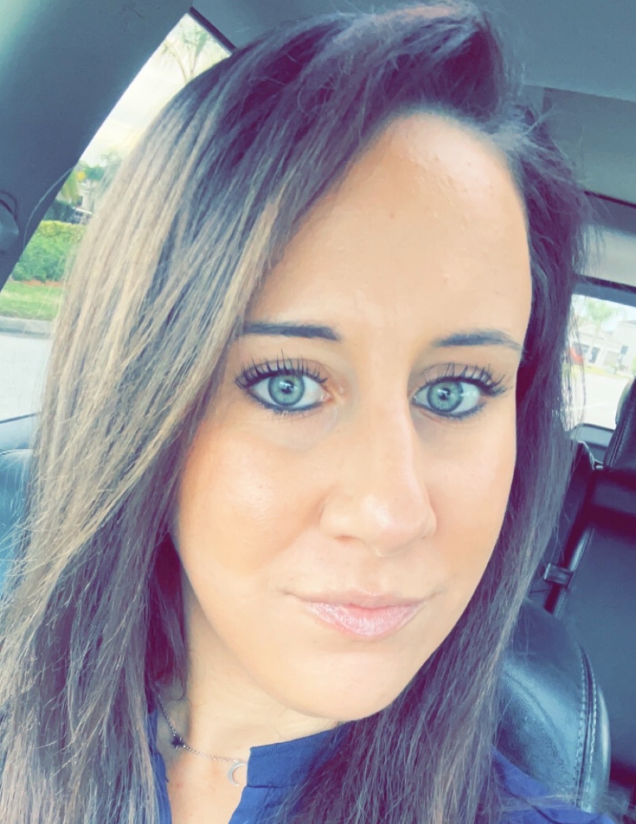 Woman with long hair and blue eyes sitting in a car, looking at the camera.