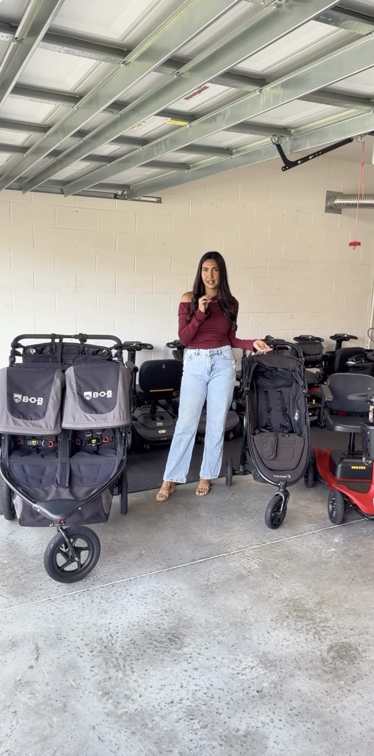 Woman standing in a parking garage with luggage and strollers, beige wall, metal ceiling, and concrete floor.