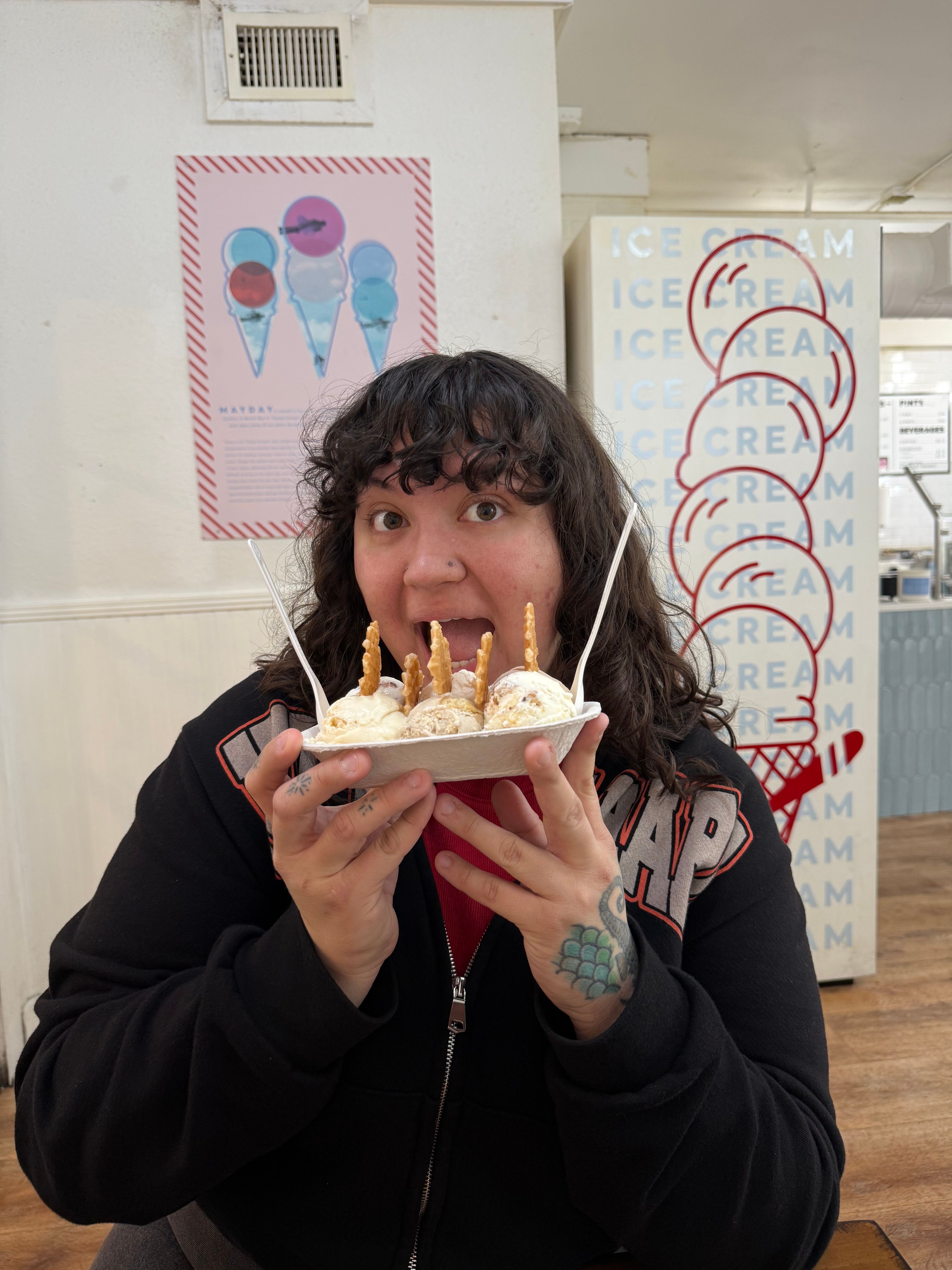 Person with dark hair and tattoos on hand holding a cake with candles, about to blow them out.