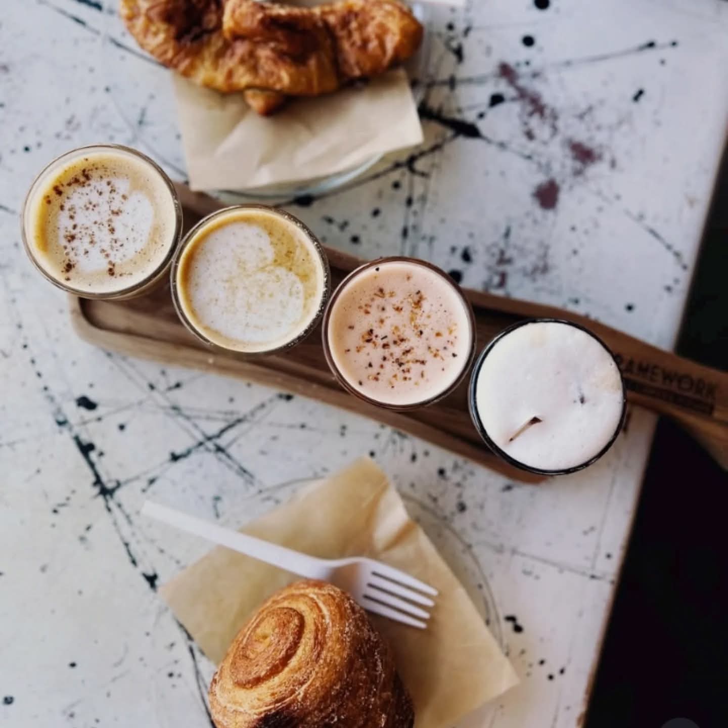 Four small glasses of different coffee drinks on a tray, with a pastry and fork on a marble table.