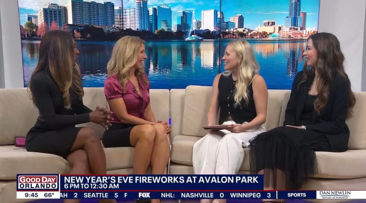 Four women sit on a beige couch in a TV studio with a city skyline backdrop, discussing New Year's Eve fireworks.