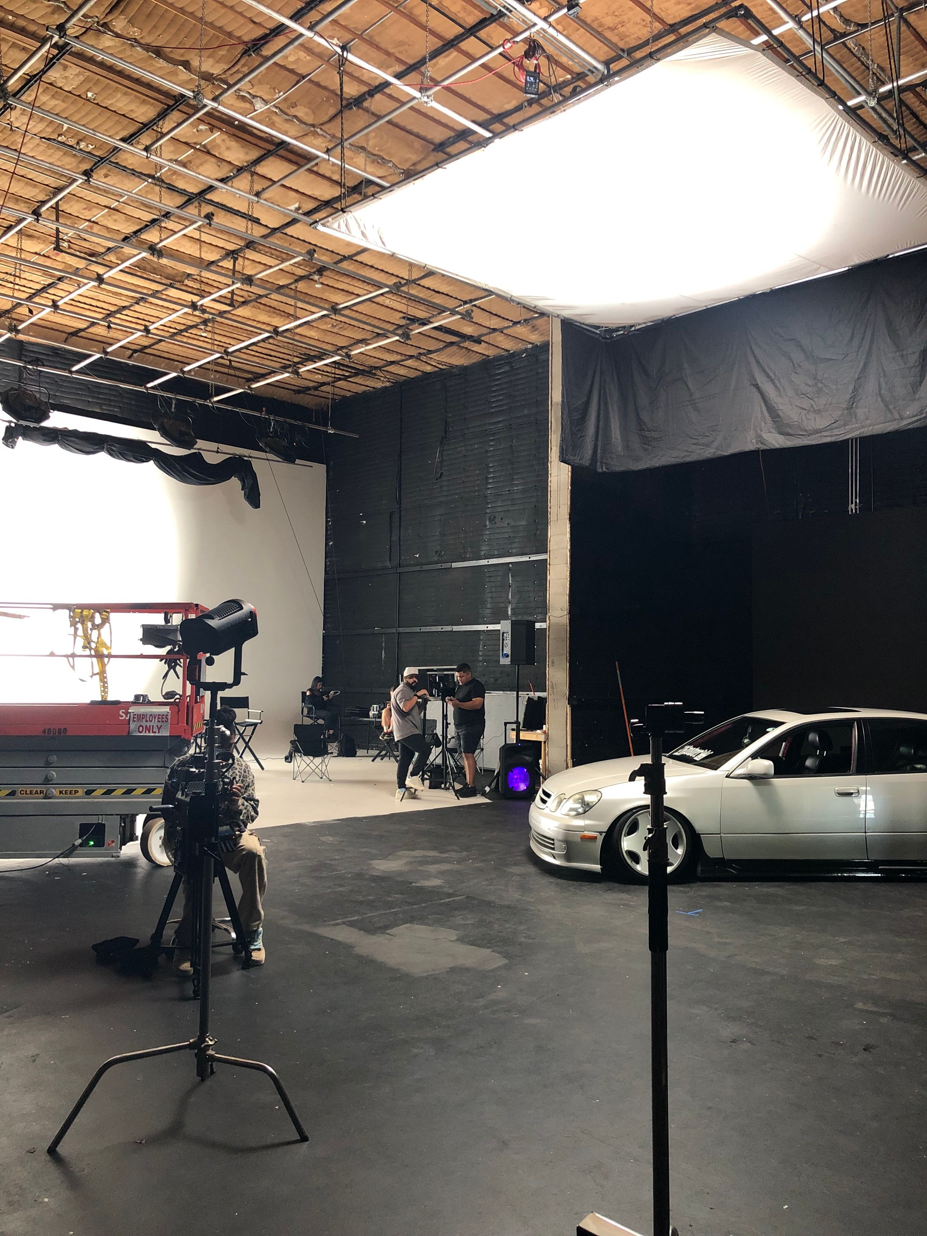 Indoor scene with a bed, motorcycle, and equipment, viewed from the side, with a tiled ceiling and dark wall.