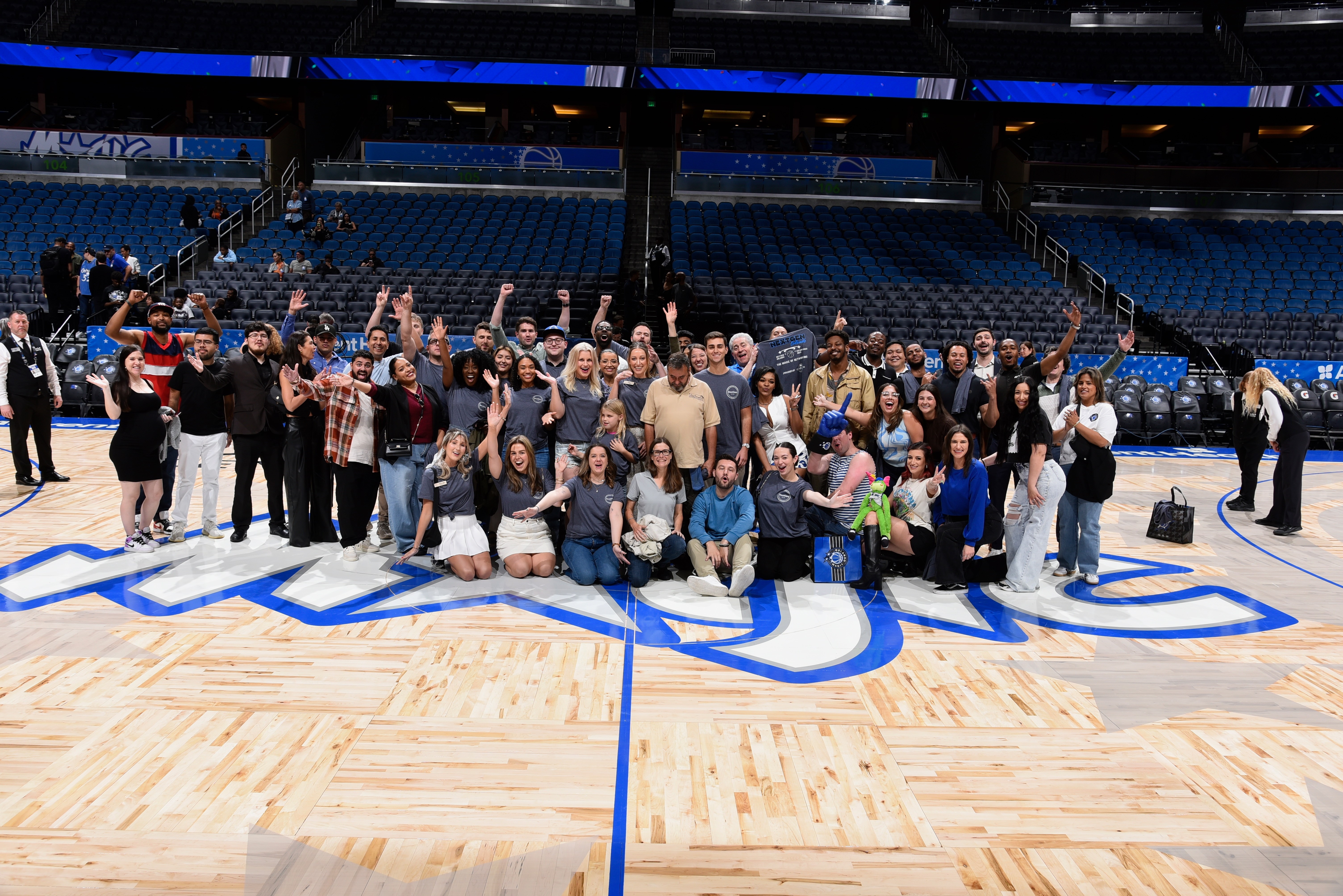Group of people standing and kneeling on a basketball court inside a stadium, posing for a photo.