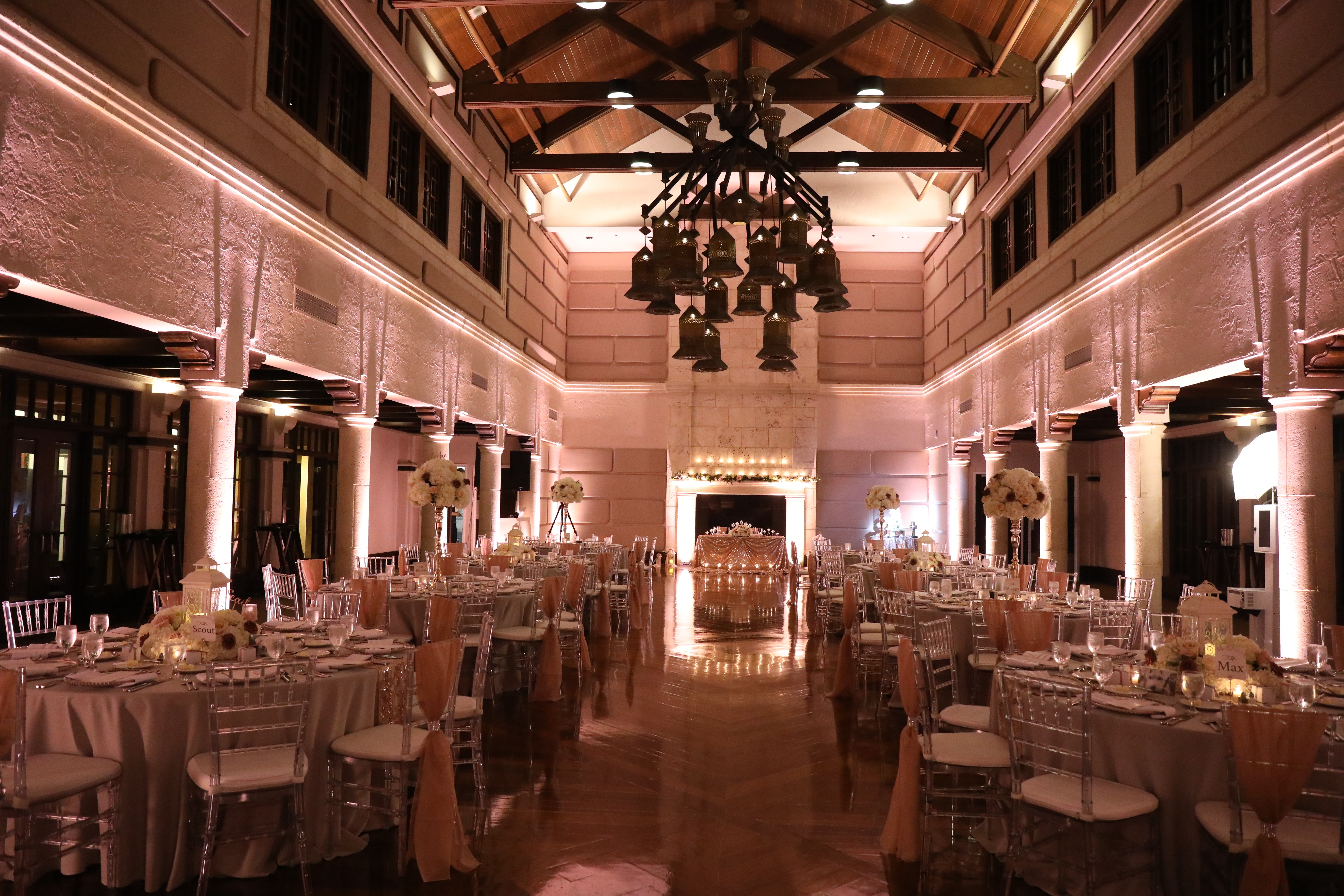 Elegant banquet hall with round tables, chairs, and a high ceiling with a chandelier, decorated for an event.