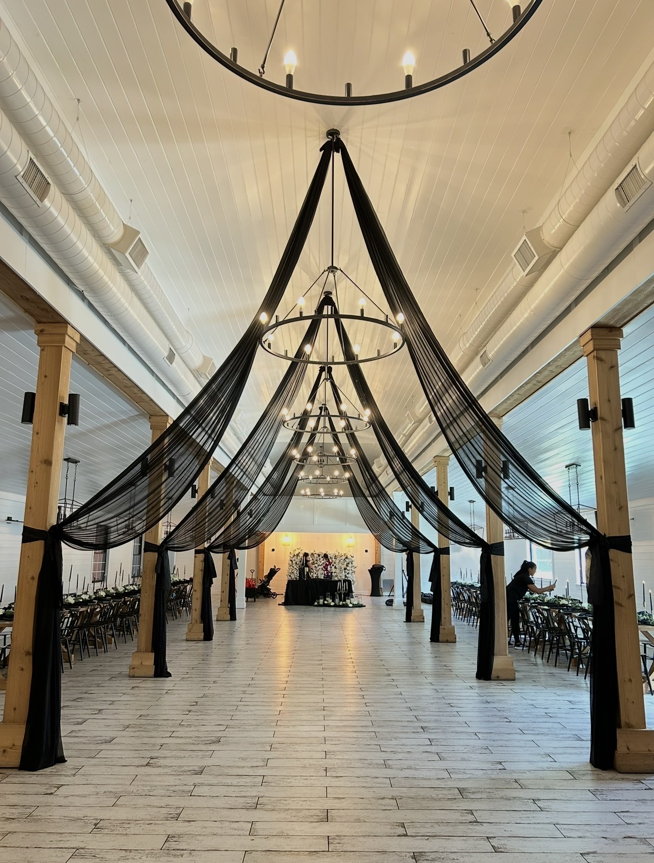 Interior space with draped black fabric hanging from the ceiling, supported by wooden columns, and large windows on sides.
