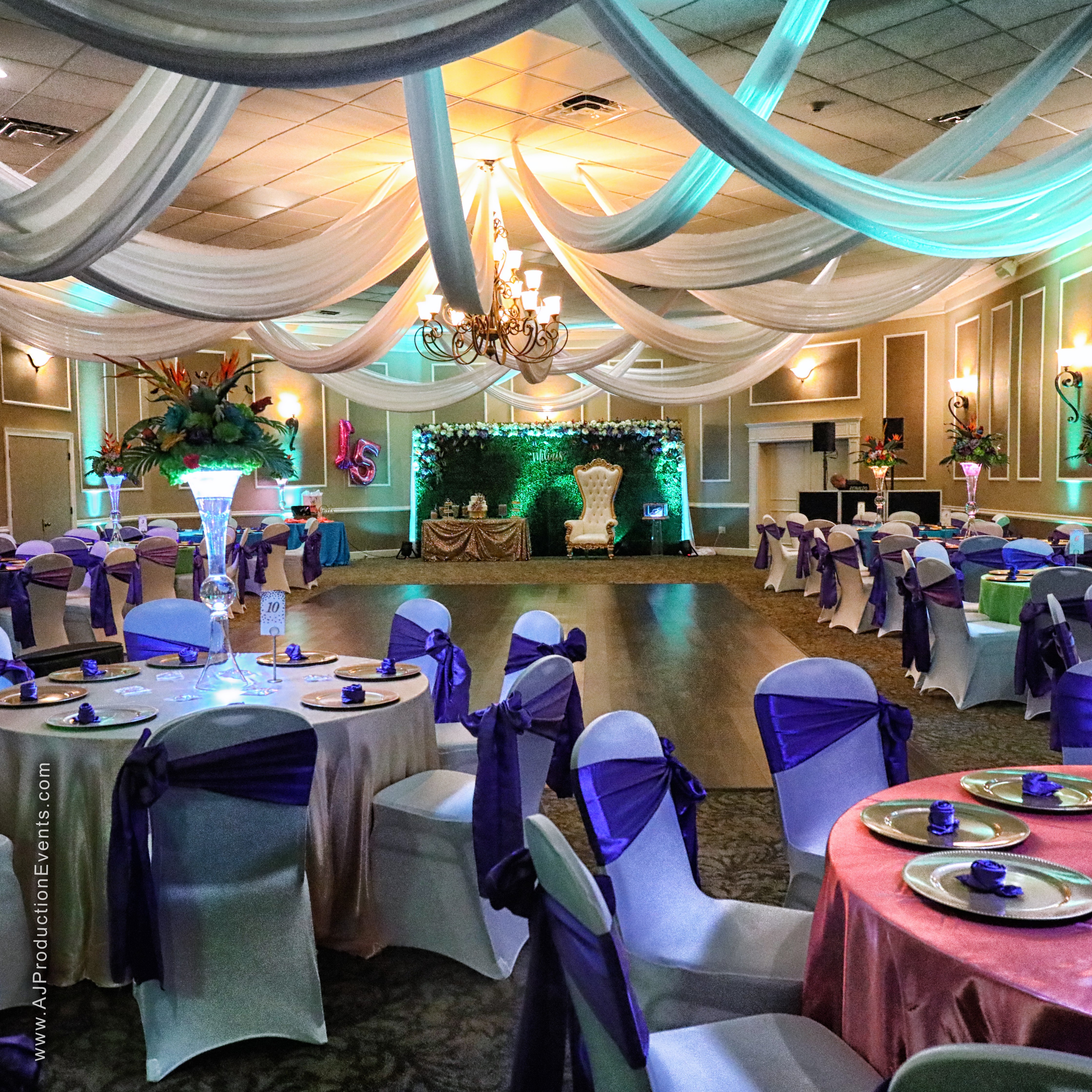 Elegant banquet hall decorated with draped fabric, chandeliers, and floral arrangements, set for a formal event with round tables and chairs.