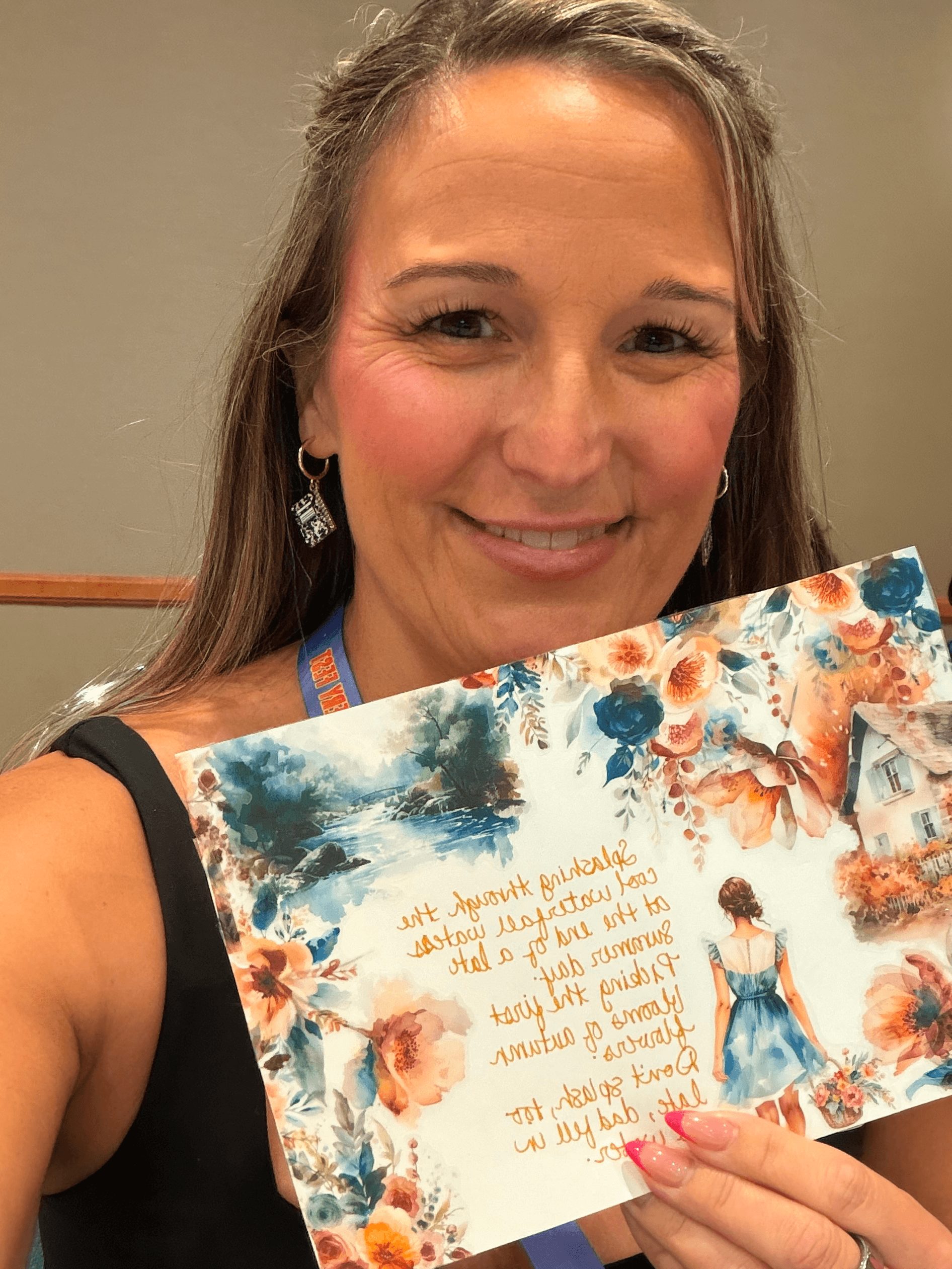Smiling woman holding a colorful card with a girl in a blue dress and floral background, indoors.