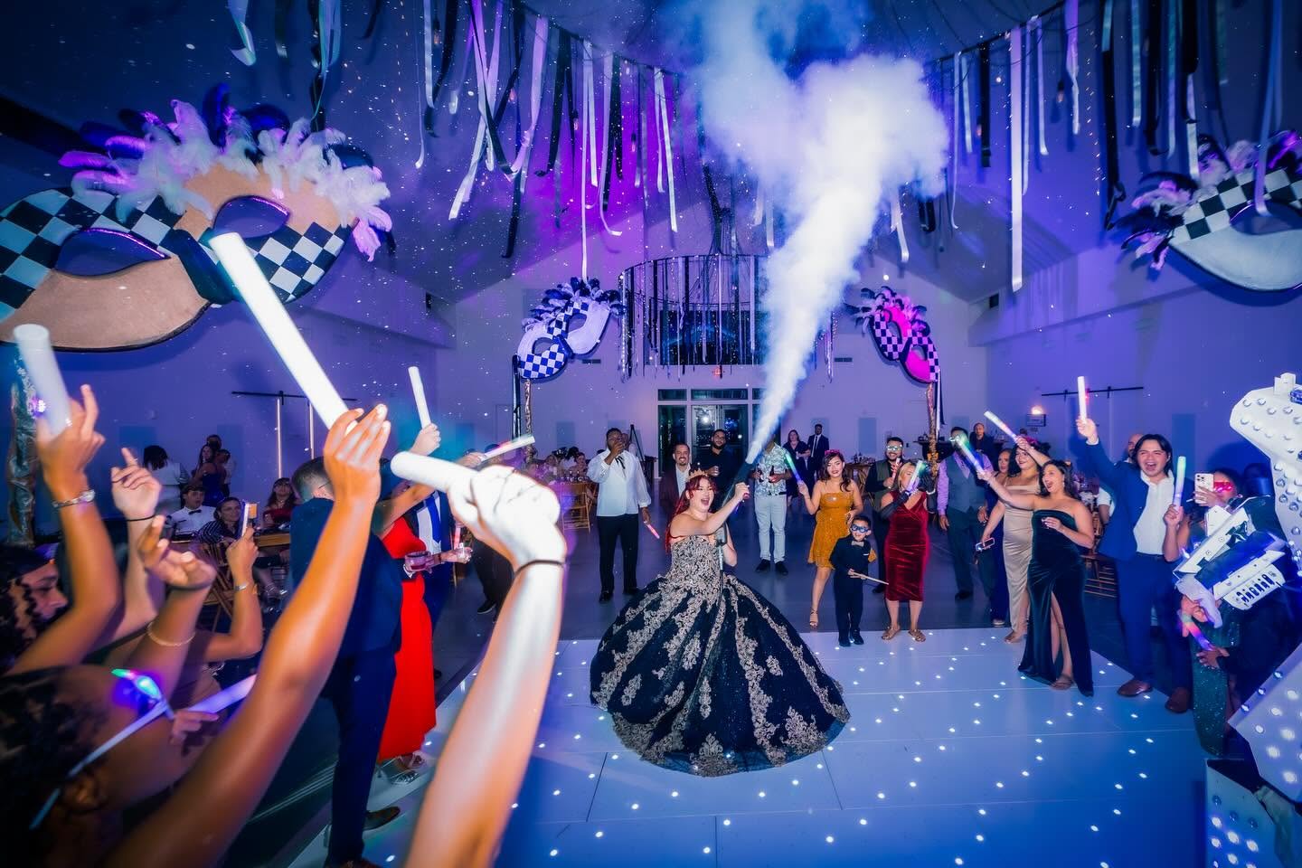 People dancing at a party with smoke and colorful decorations, some holding glow sticks, in a lively indoor setting.