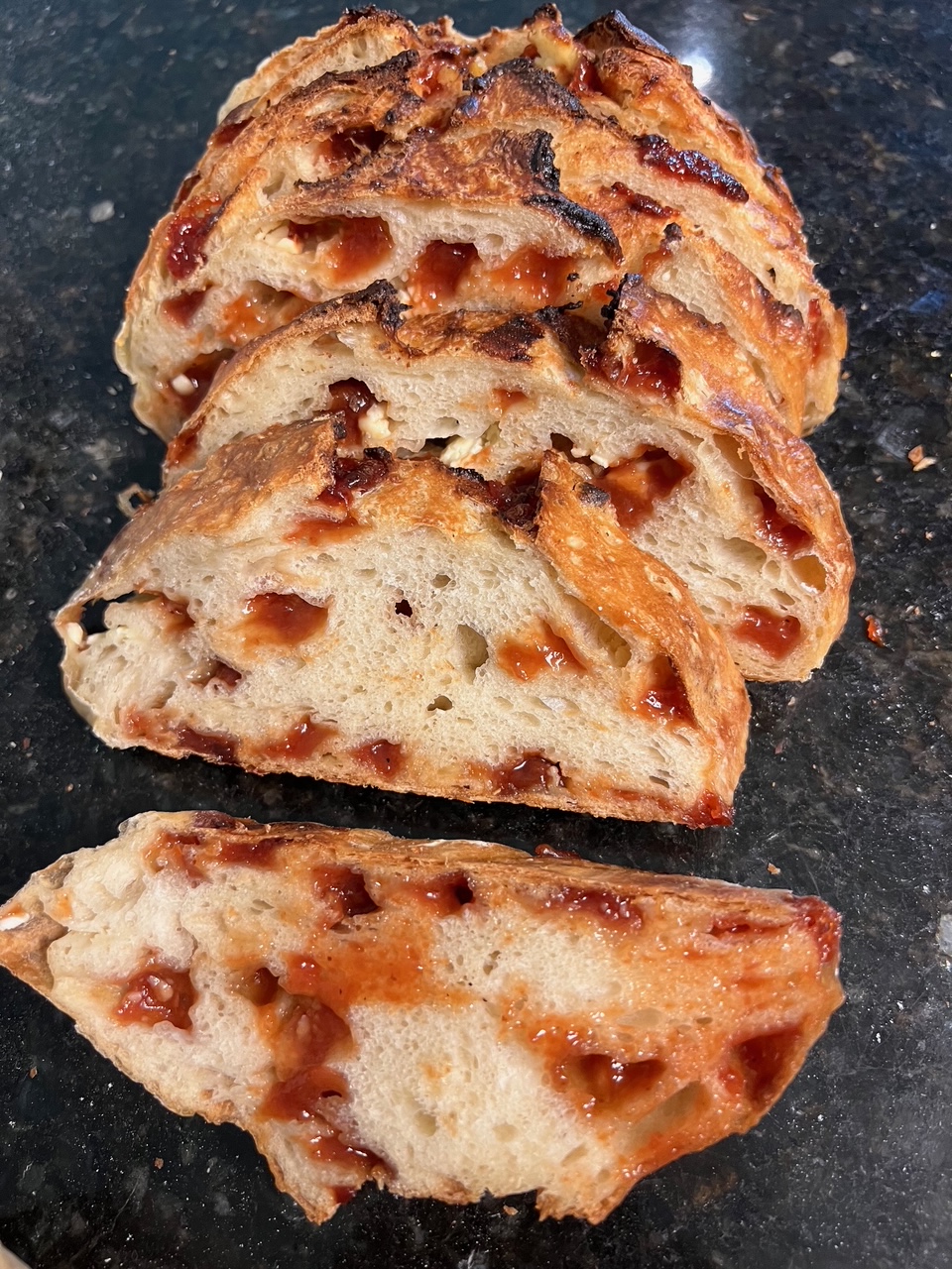Sliced bread with a golden crust and visible fruit pieces inside, on a dark surface.