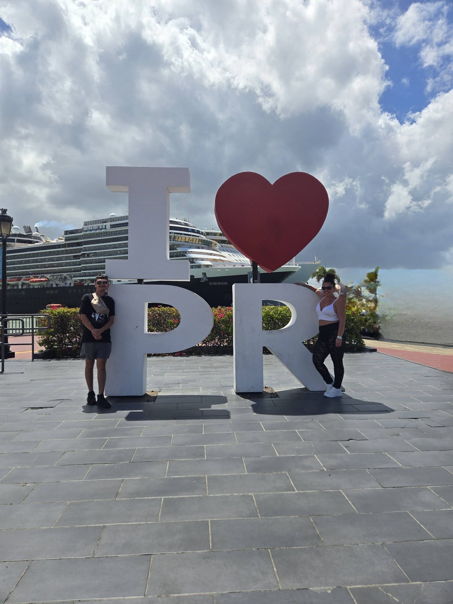 Two people stand beside large white letters spelling 'I', 'D', and 'R' with a red heart between 'I' and 'D'.