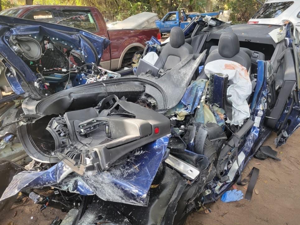 Damaged convertible car with deployed airbags and crushed interior after an accident, surrounded by other vehicles.