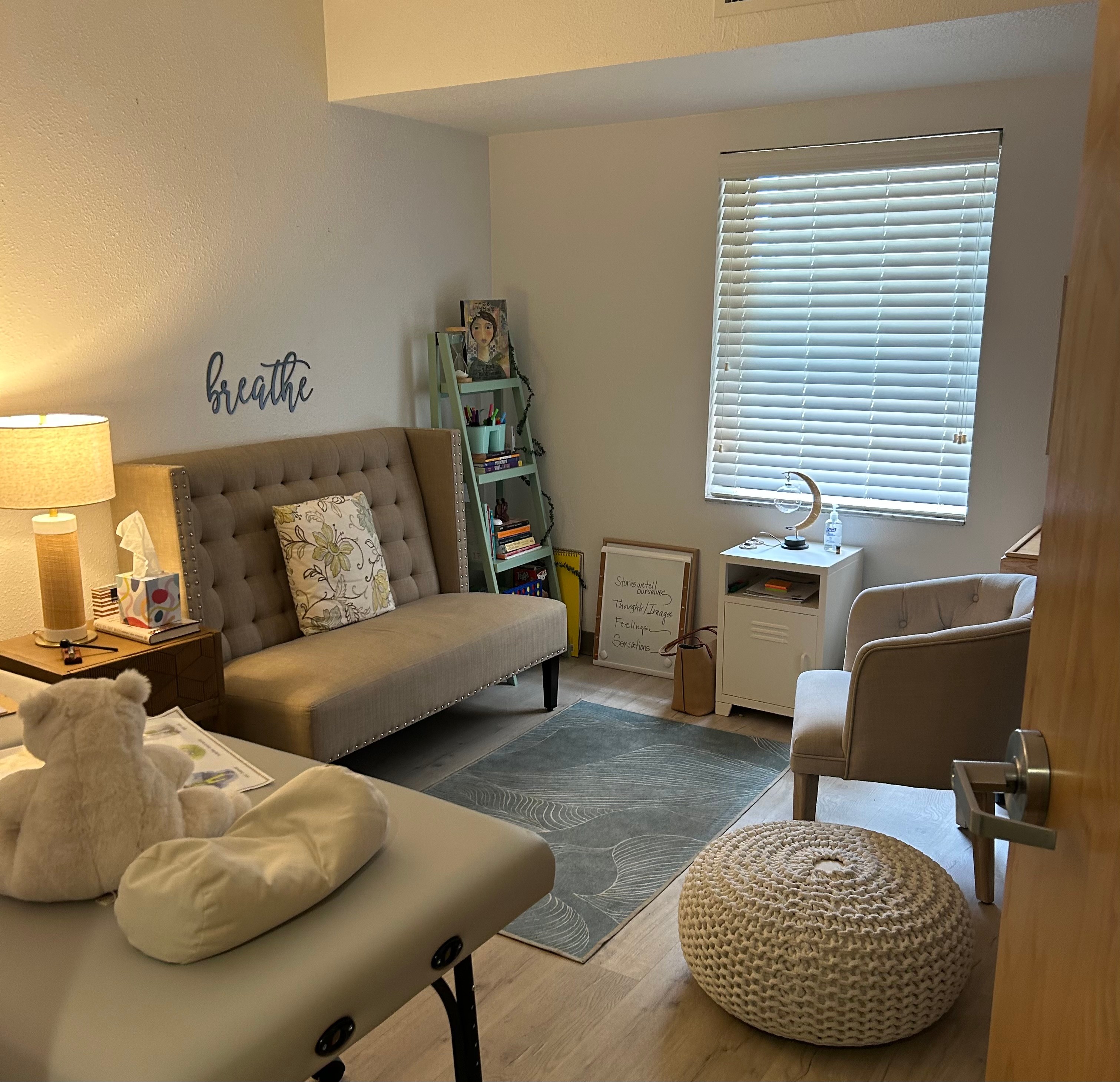 Room with a beige tufted sofa, armchair, window with blinds, and decorative items including a sign that says 'breathe'.