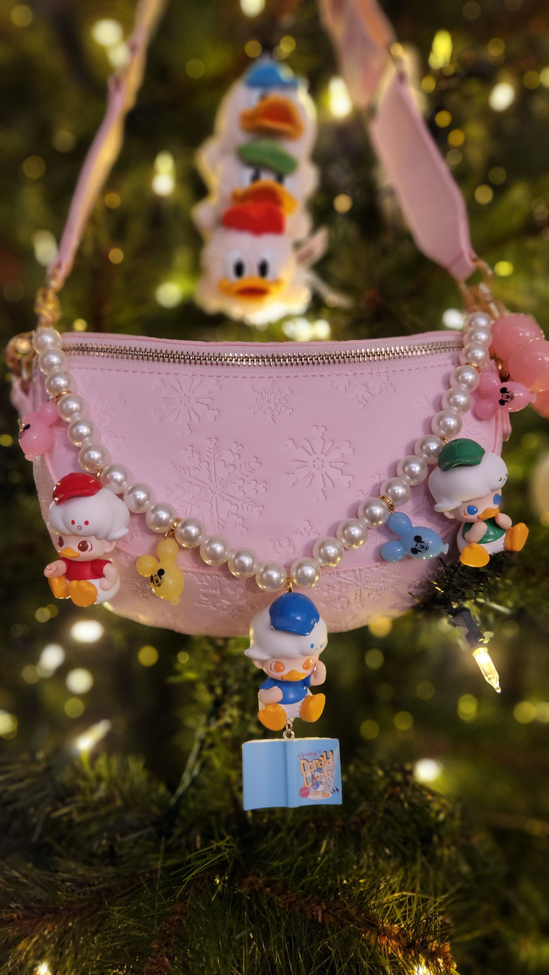 Pink purse decorated with pearl beads and small colorful toys, hanging on a Christmas tree branch.