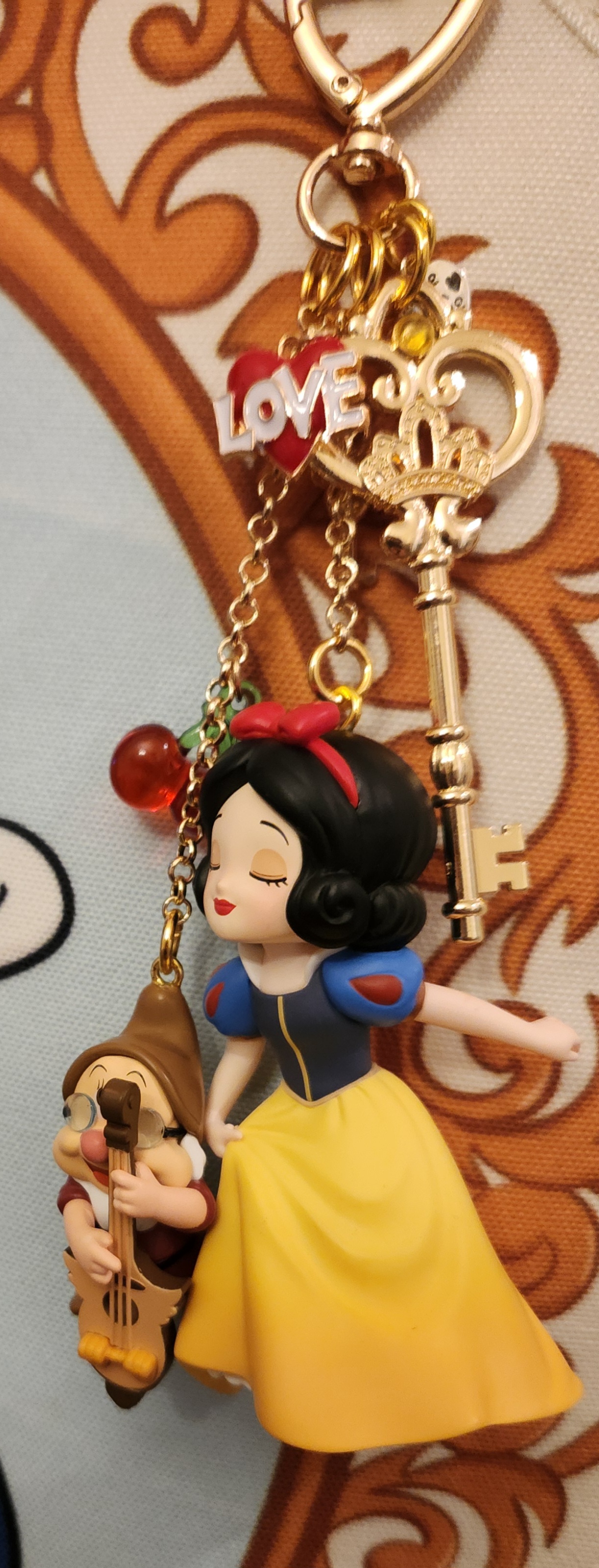 Snow White keychain with a figure holding a small animal, gold key, and a red and green bead, against a wooden background.