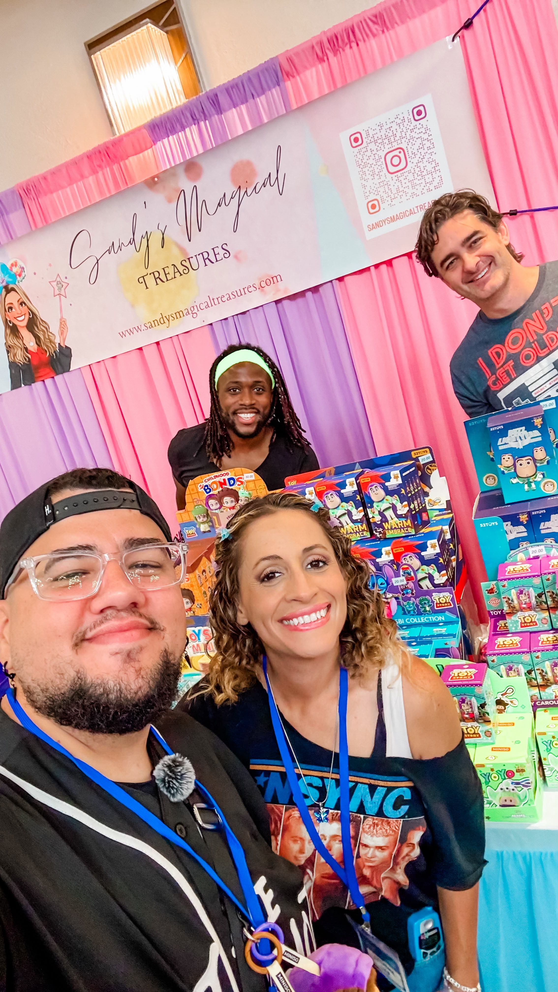 Four people smiling at a booth with colorful toys and a sign that reads 'Super Magical Treasures.'