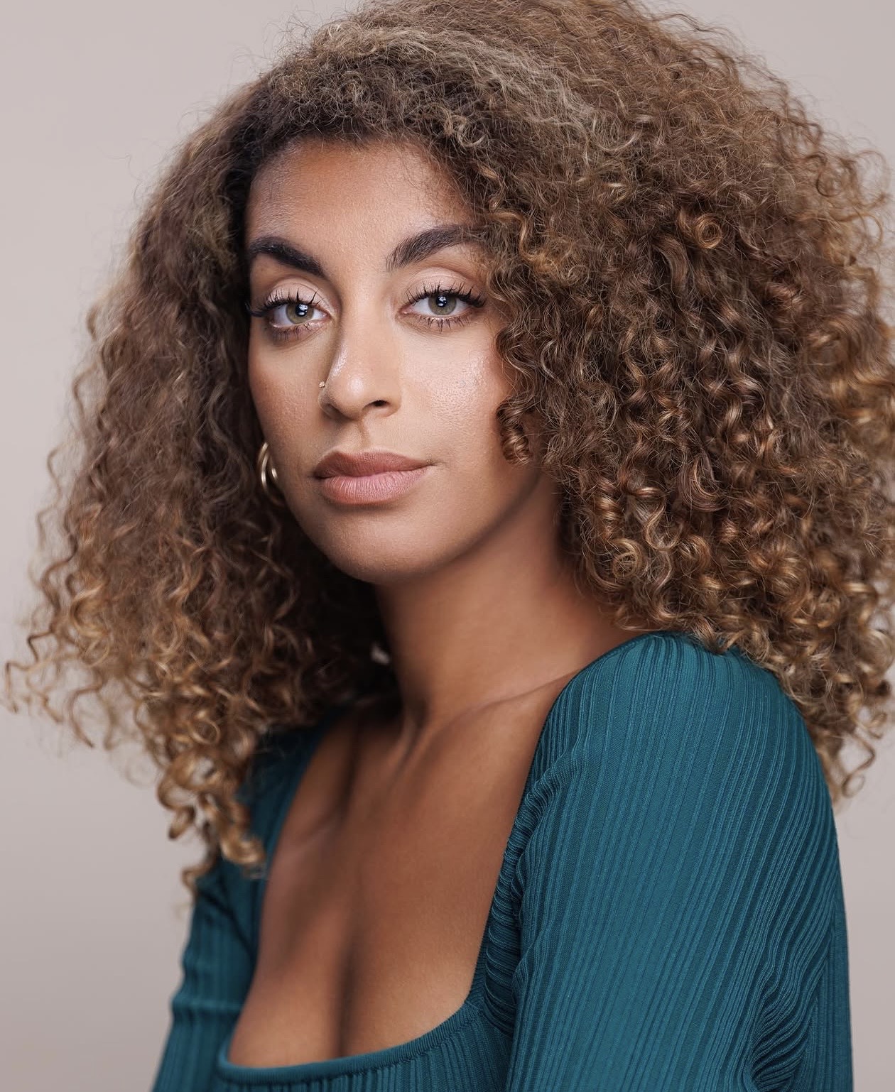 Portrait of a woman with curly hair wearing a teal top, looking at the camera with neutral expression.