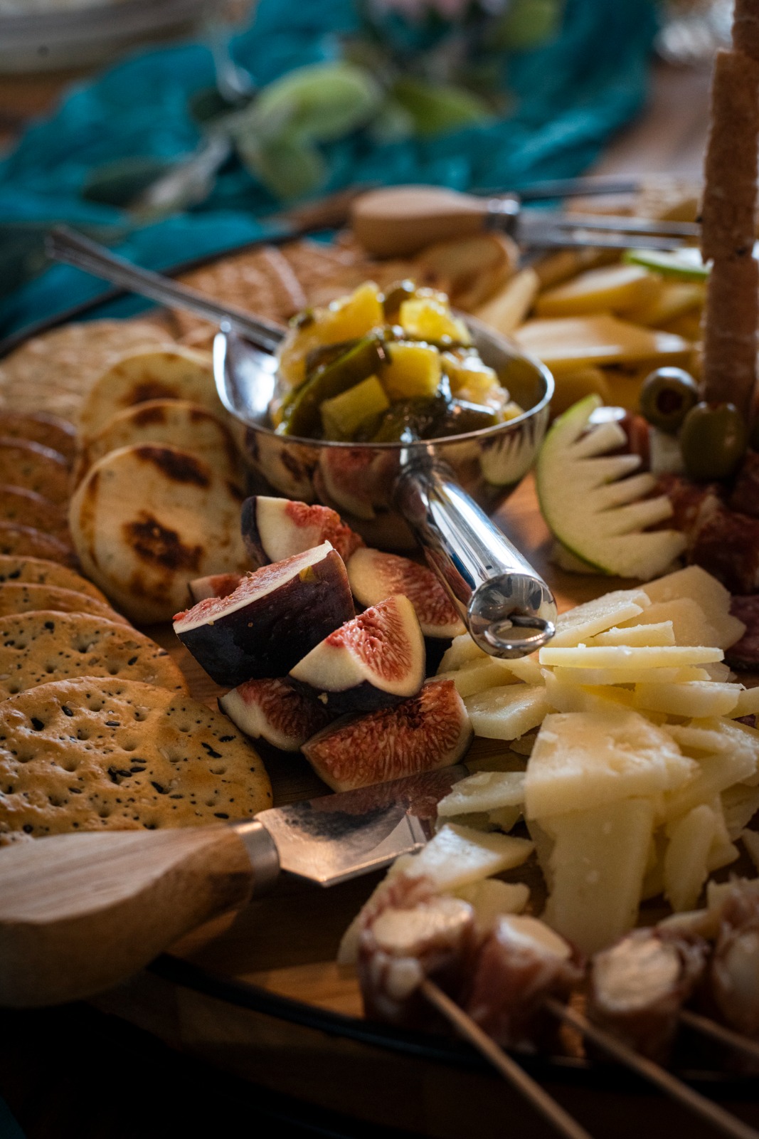 Cheese, bread, figs, olives, and pickles on a wooden platter, with a fork and a bowl of pickles in the center.