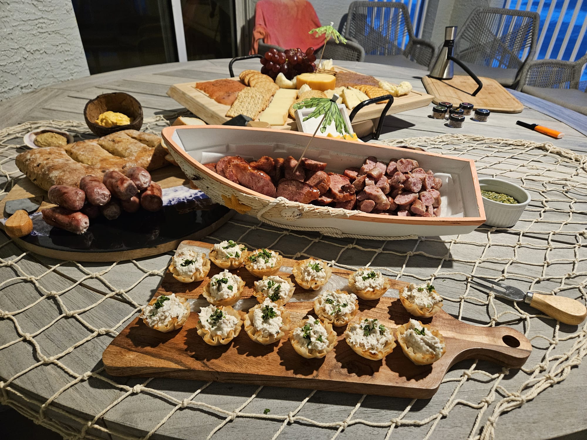 Table with various appetizers and snacks, including sushi, bread, and small dishes, on a round table with a netted tablecloth.