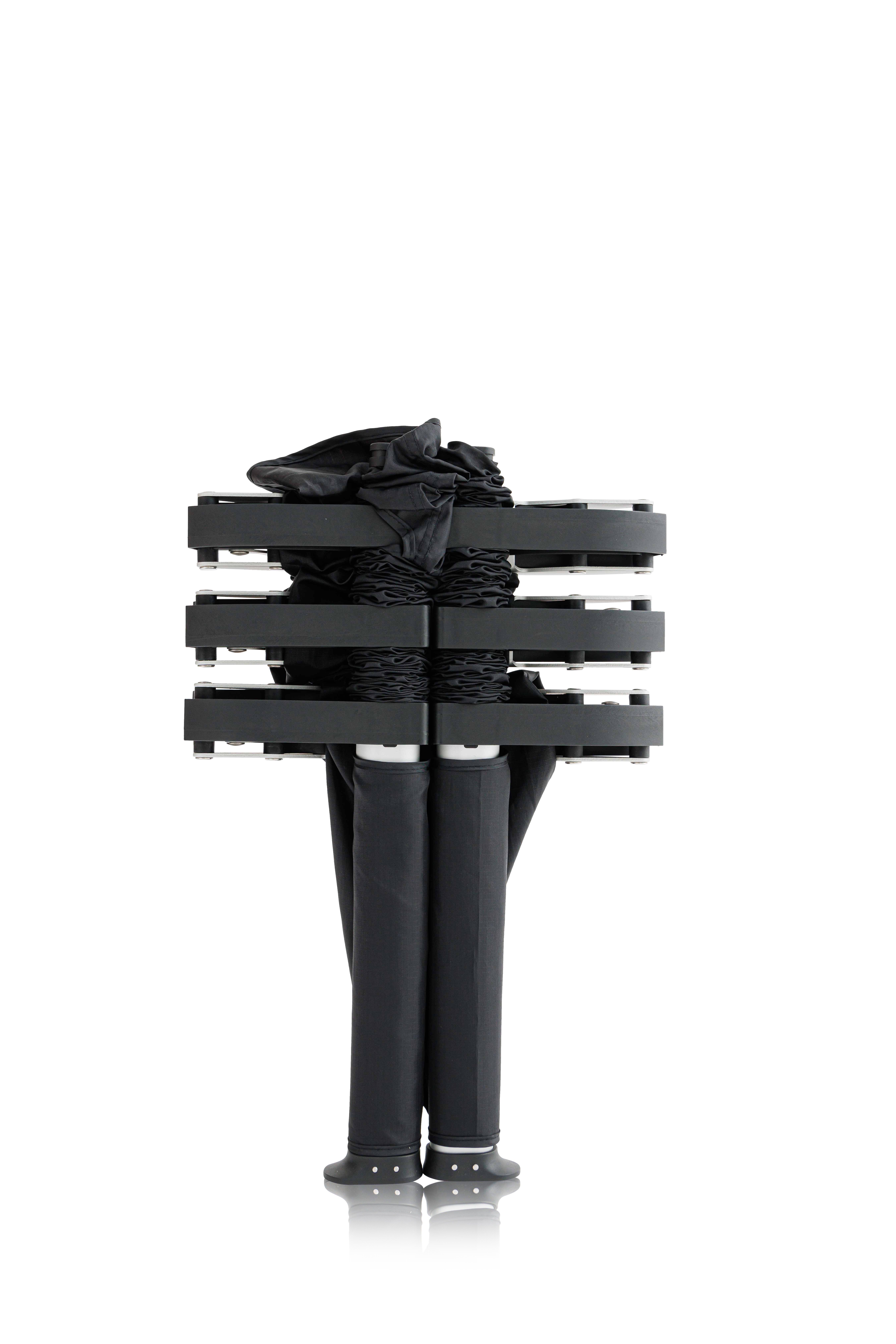 Stacked black chairs with a black bag on top, viewed from the side, against a white background.