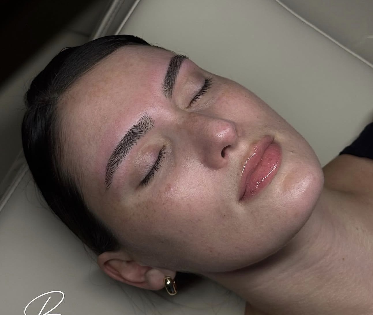 Close-up of a woman with closed eyes and smooth skin, lying down with her head tilted back.