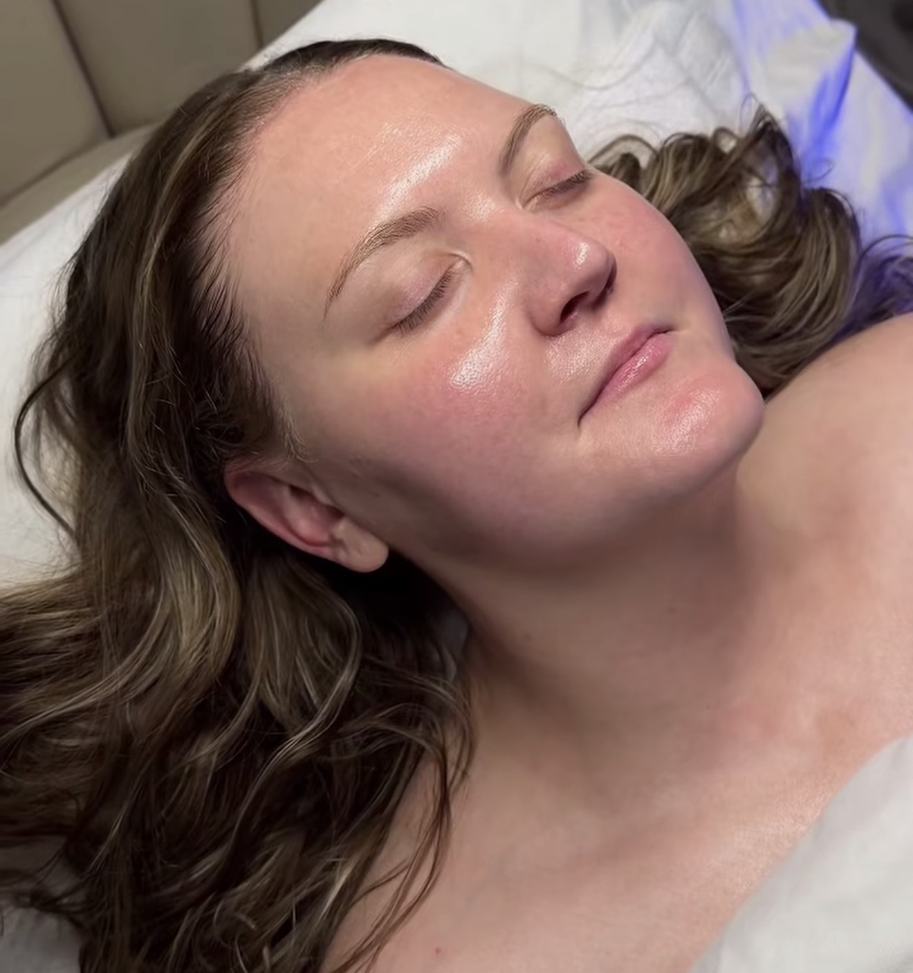Woman with closed eyes lying on a bed, with long hair and relaxed expression.
