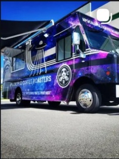 Bus with galaxy-themed design and Star Wars logo, parked outdoors under a blue sky.