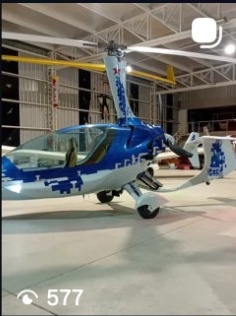 Small helicopter with blue and white pixelated design, displayed indoors on a concrete floor.