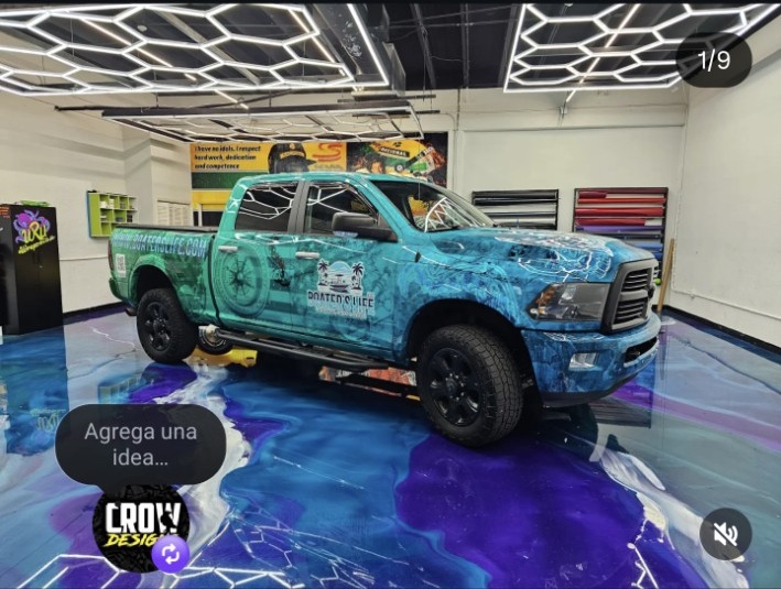 A blue and green truck with a logo on the door is displayed indoors on a colorful floor.