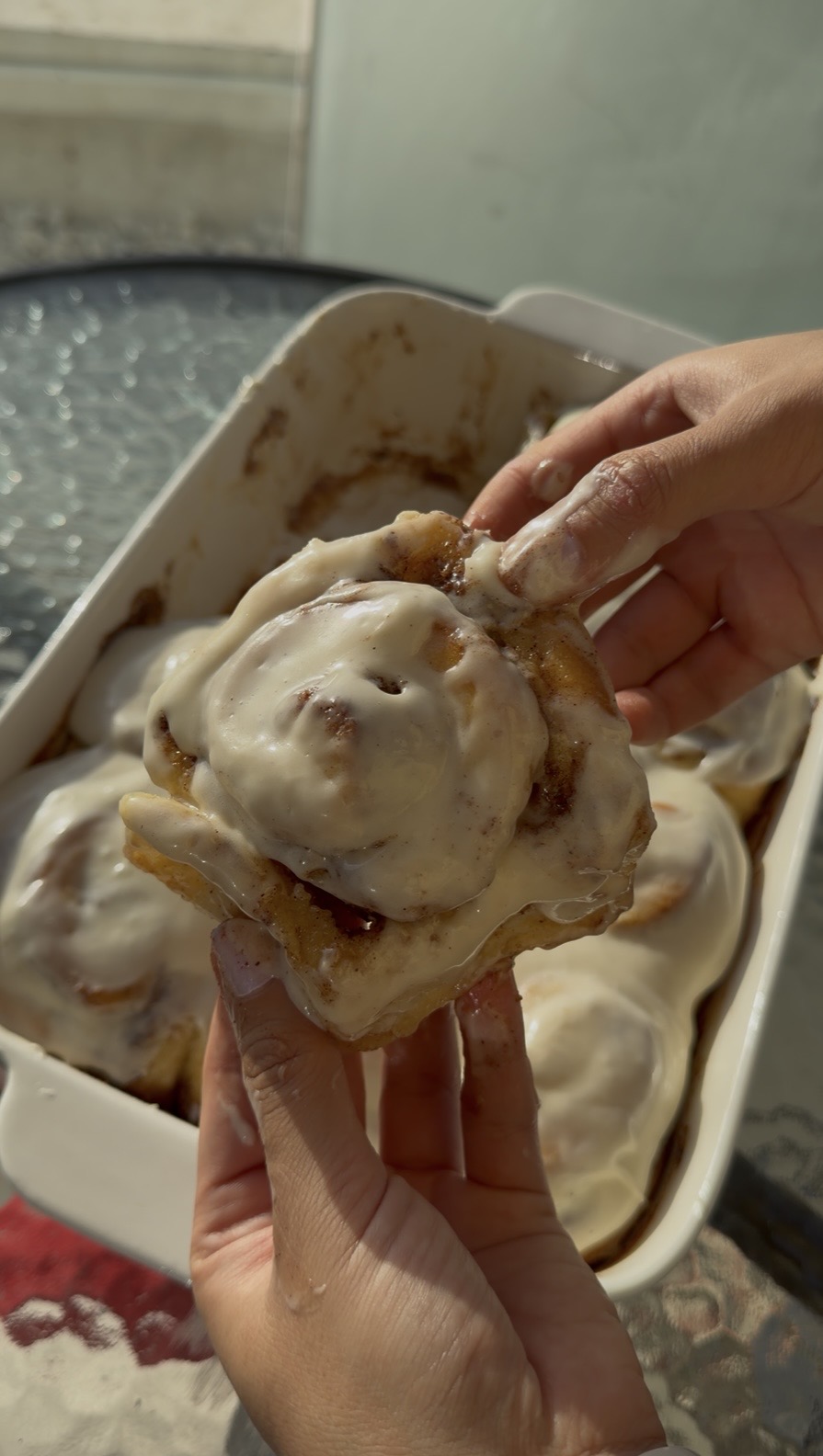 Person holding a scoop of ice cream on a cookie, with a container of ice cream in the background.