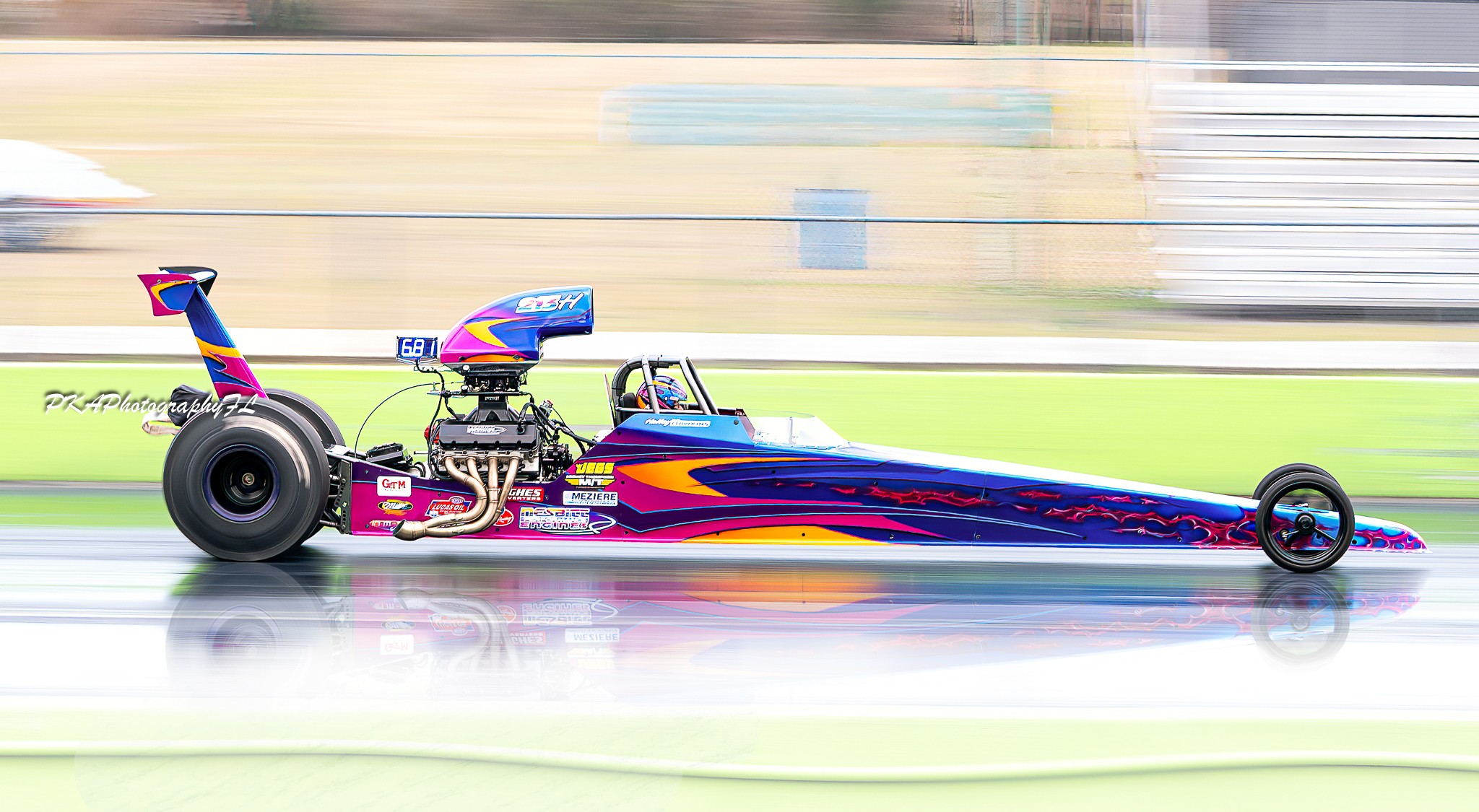 Colorful drag racing car on track with blurred background, showing motion and speed.