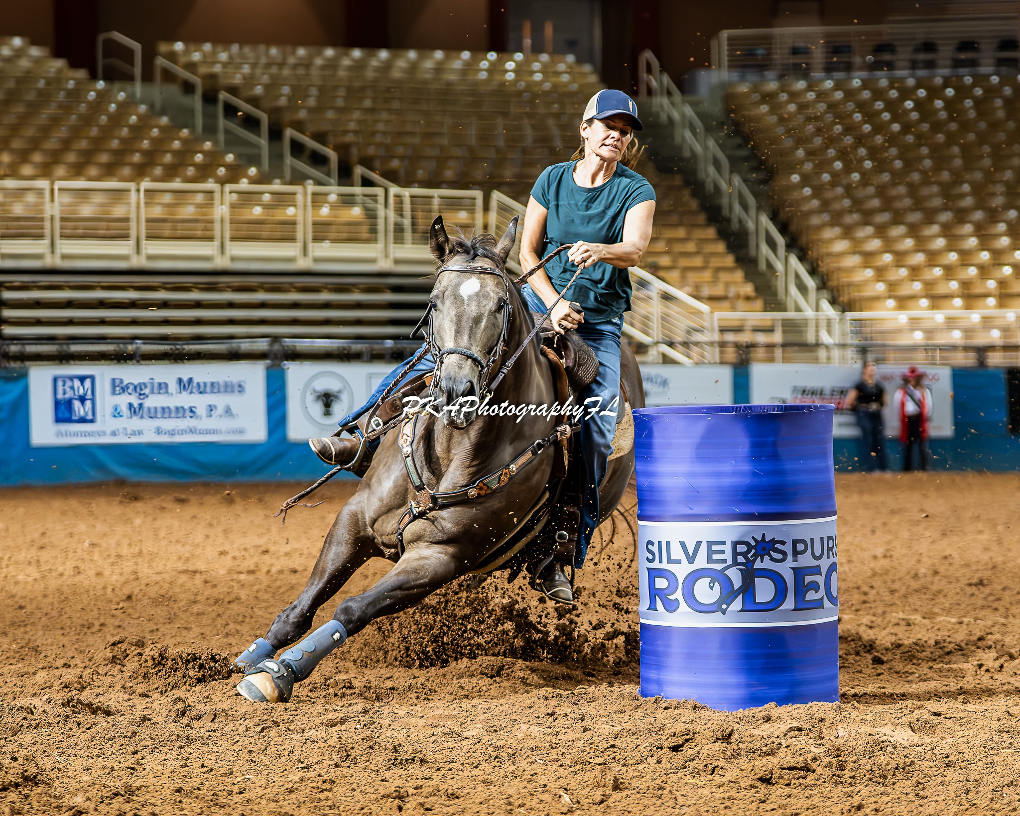 Person riding a horse around a barrel in an indoor arena, with empty seats in the background.