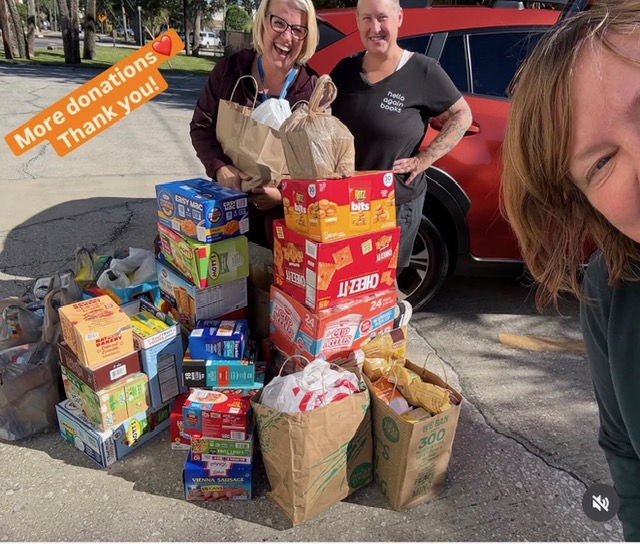 Three people with grocery and donation bags outdoors, smiling, with a red vehicle behind them, and a sticker saying 'More donations Thank you!'.