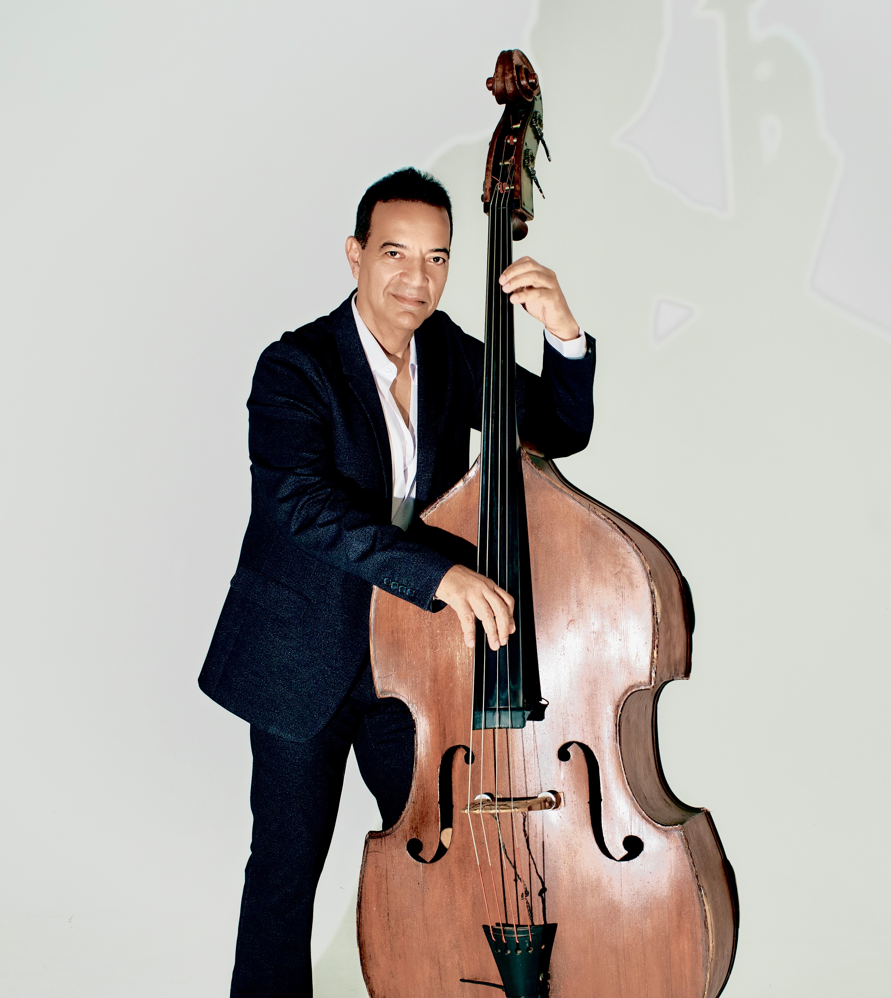 Man in a dark suit holding a double bass, standing against a plain light background.