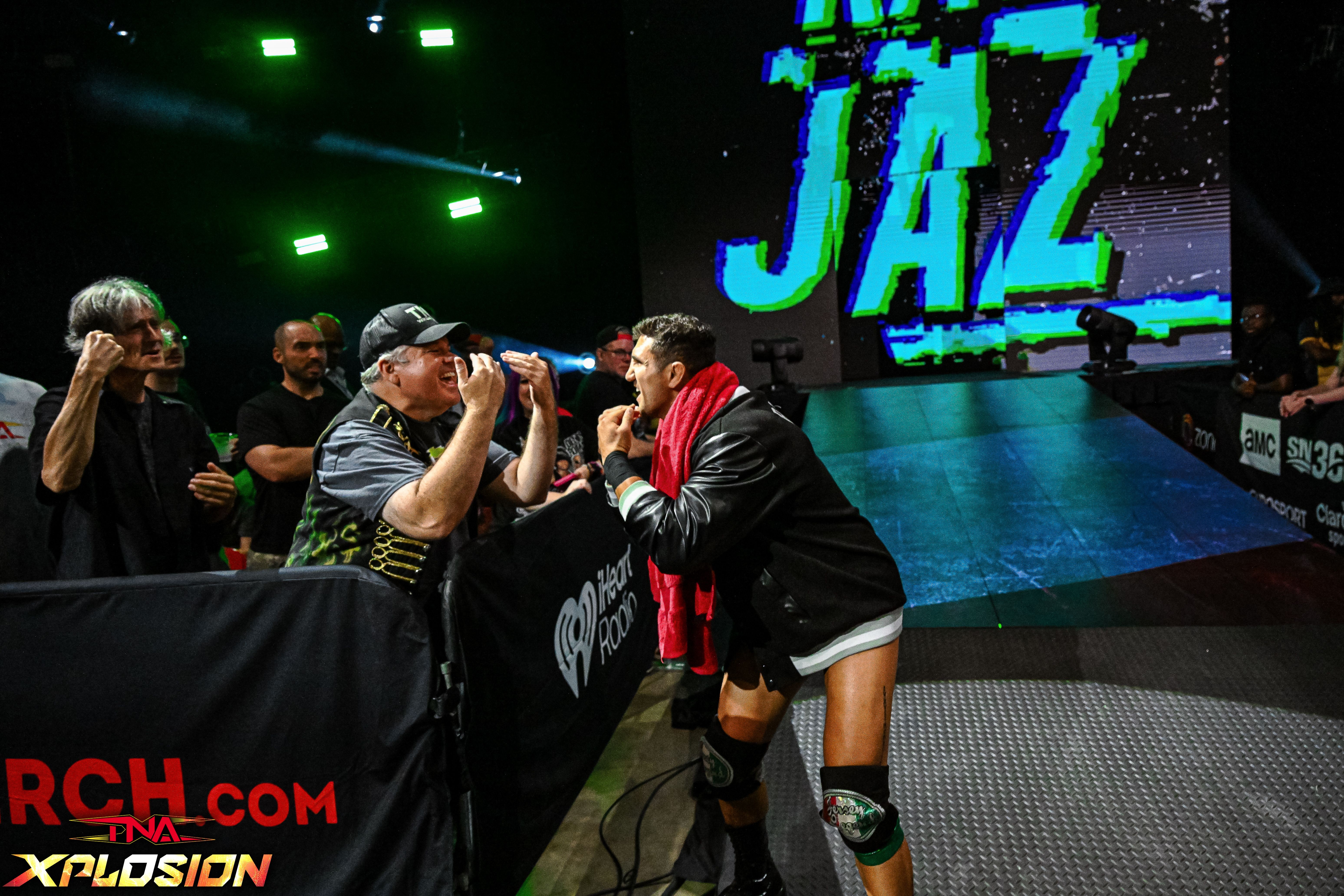 Wrestler interacts with fans at a wrestling event, with a large screen displaying 'JAZ' in the background.