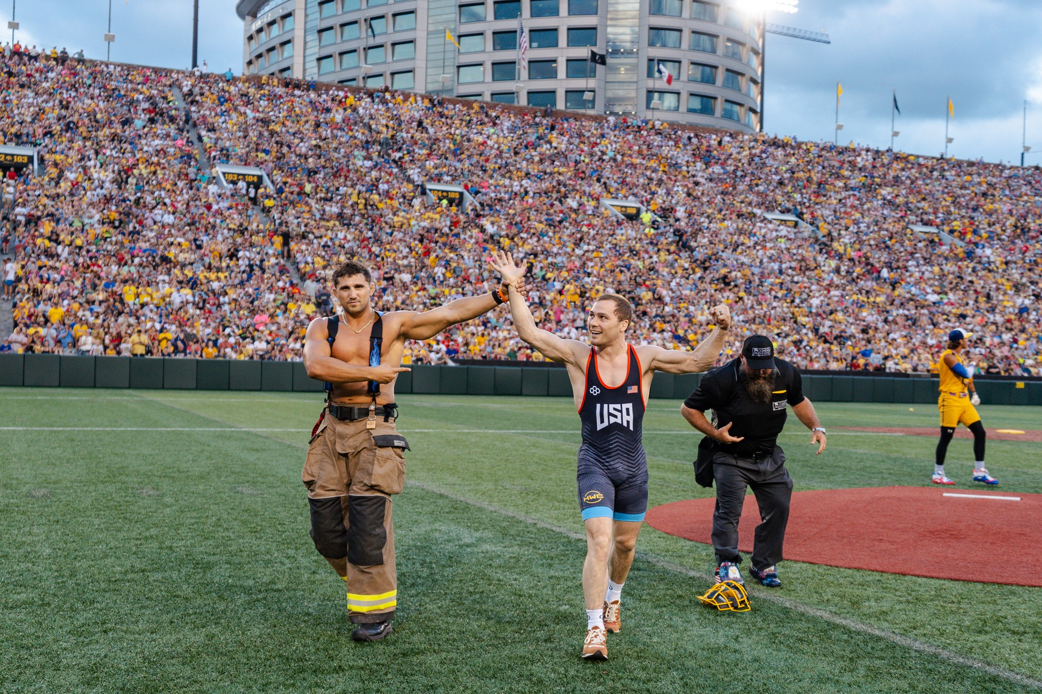 Person in a USA sports jersey high-fives a person in a brown costume on a sports field, with a large crowd in the background.